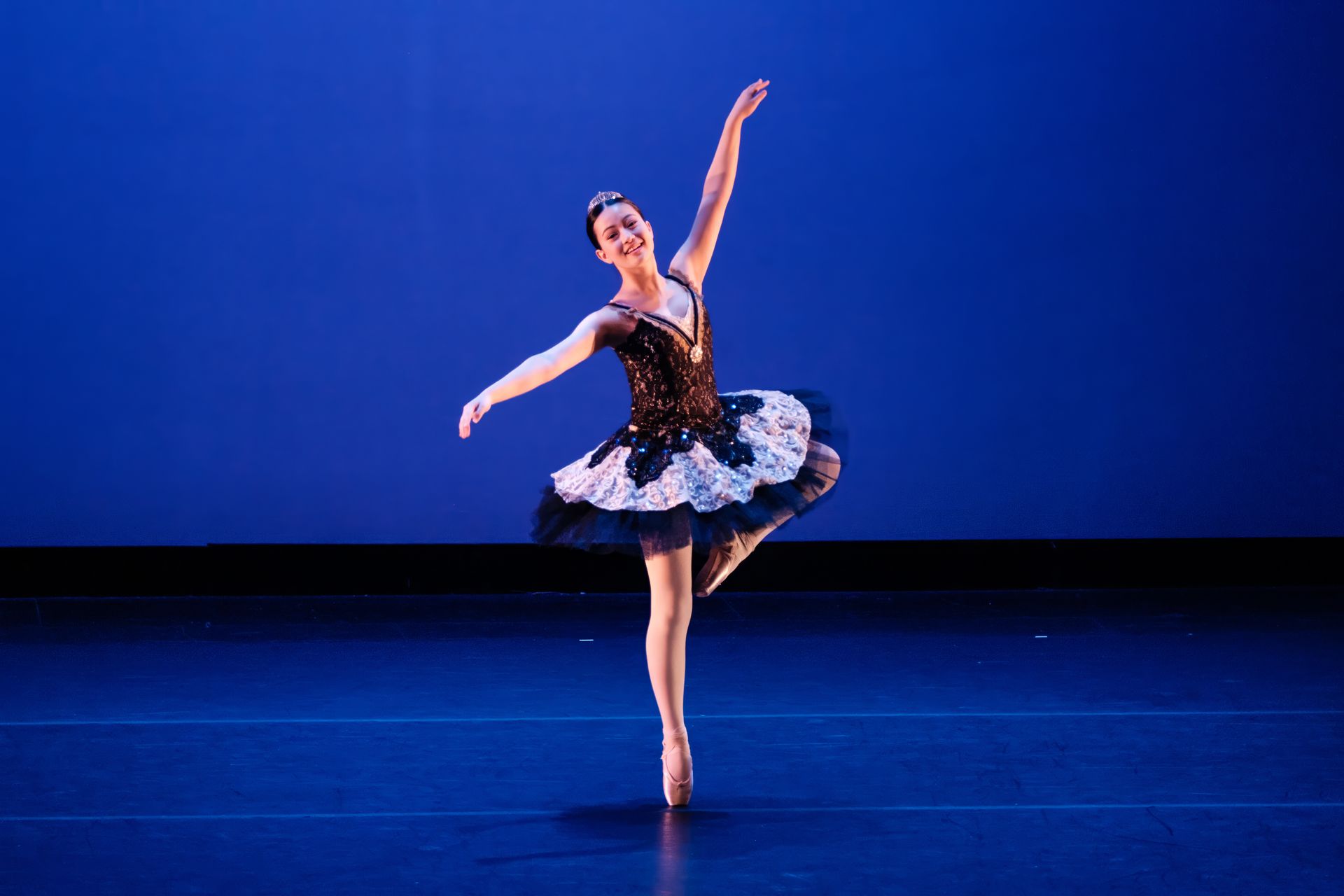 Ballet dancer in black and blue tutu posing on stage against a blue backdrop