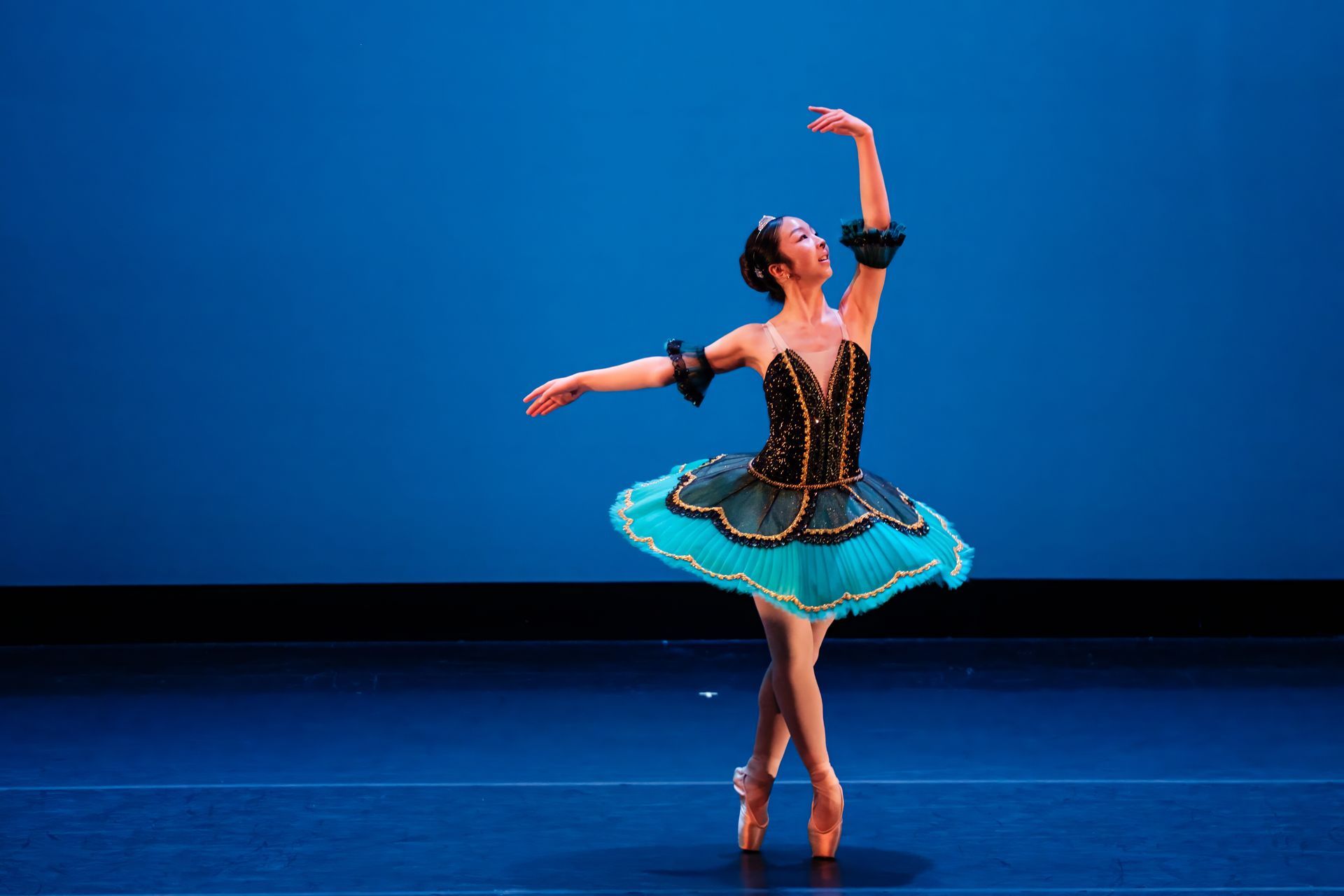Ballet dancer in a black-and-turquoise tutu posing on a blue-lit stage