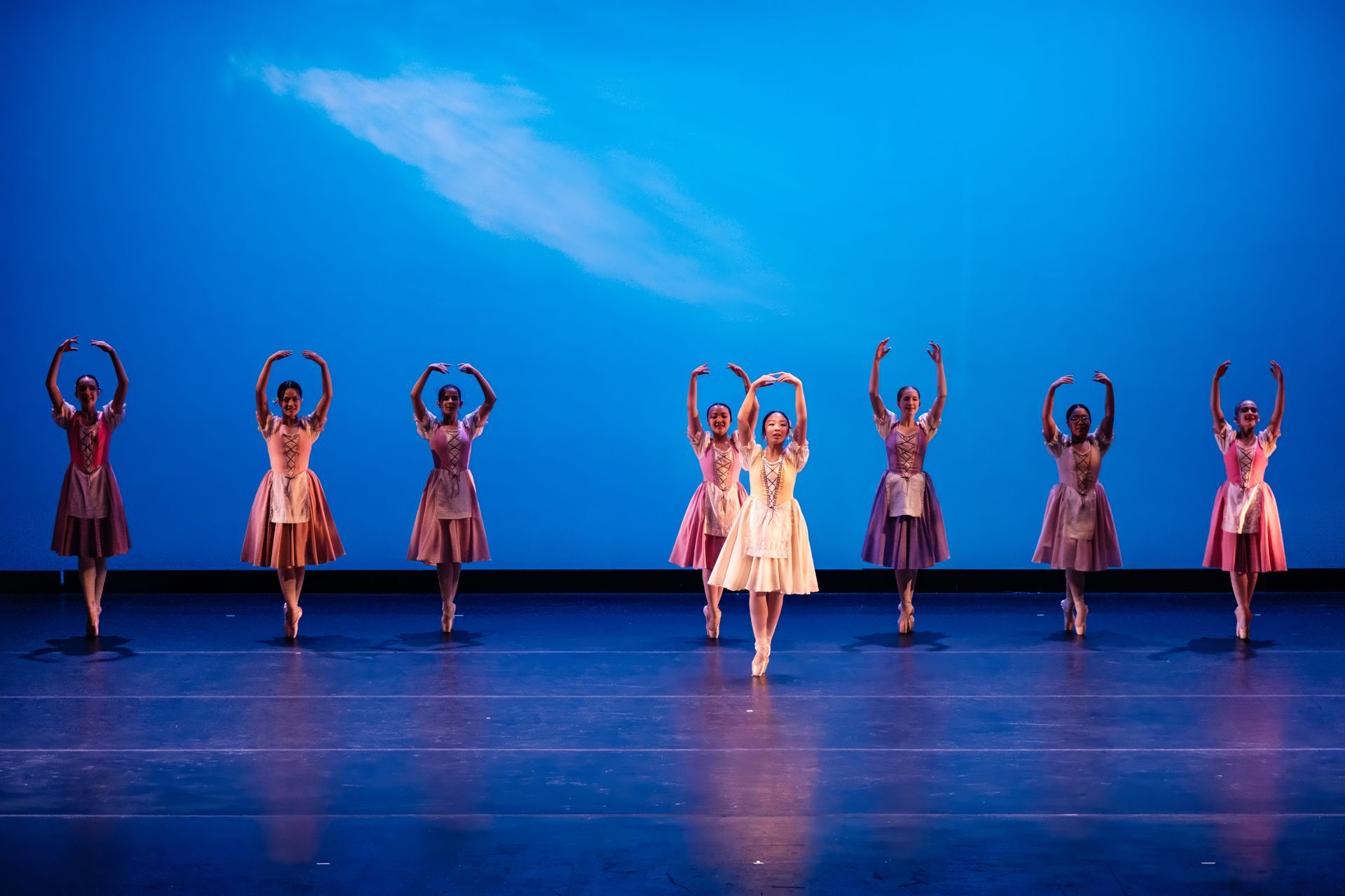 Dancers in colorful costumes perform with raised arms on a blue-lit stage