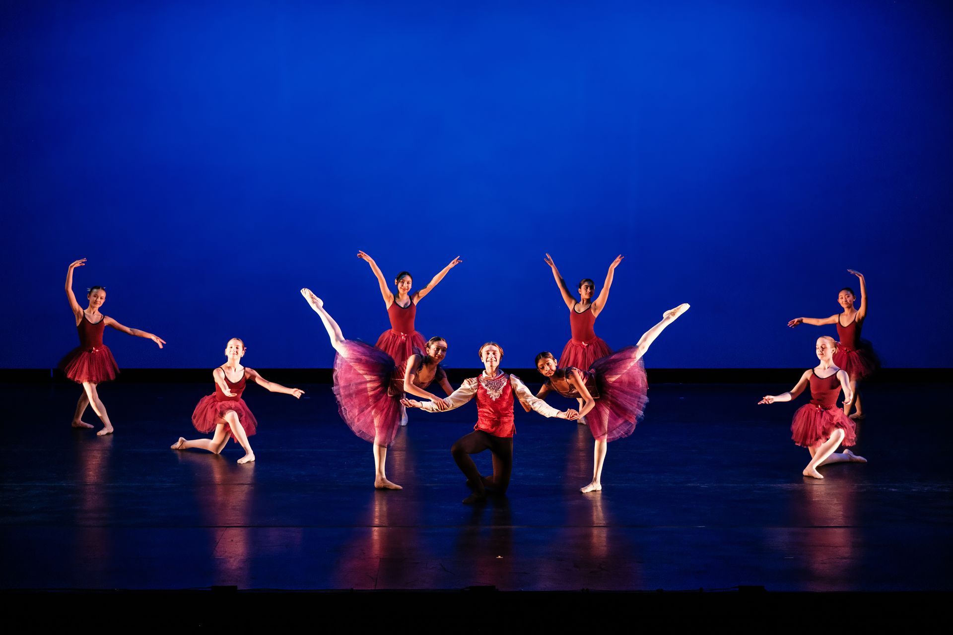 Ballet dancers in red costumes performing a synchronized routine on a blue-lit stage