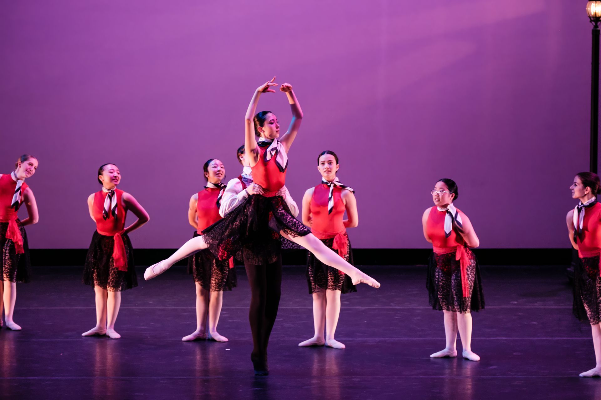 Ballet dancers in red and black costumes performing onstage under purple lighting
