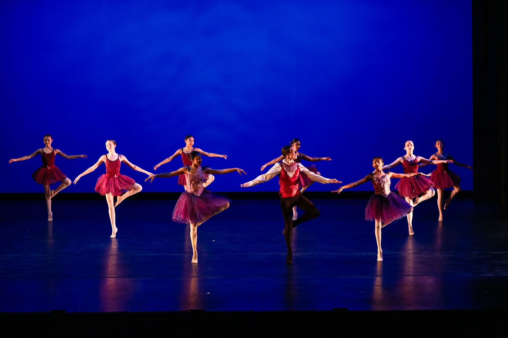 Six dancers in red costumes perform a synchronized routine on a blue-lit stage.