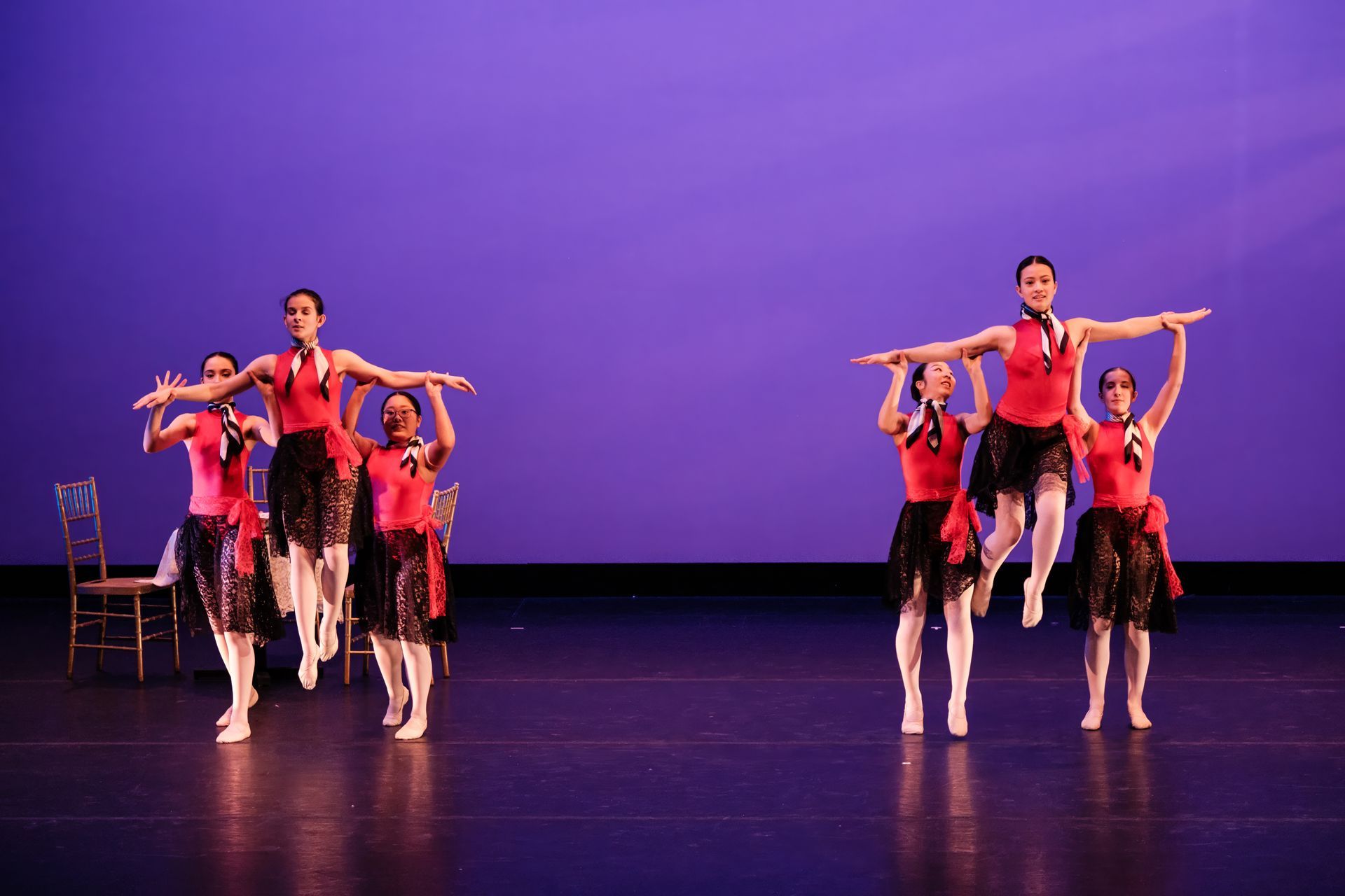 Ballet dancers in pink and black costumes perform on a purple-lit stage, two pairs in the foreground