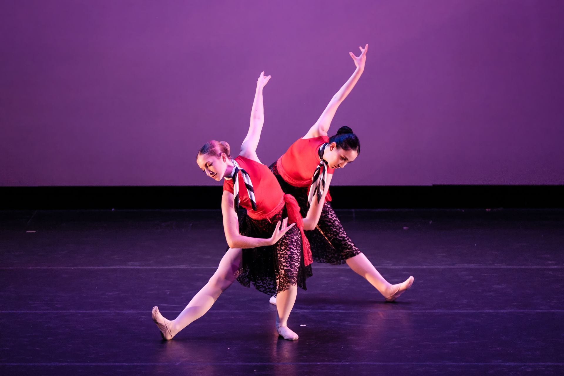 Two dancers in red costumes posing on a stage with a purple backdrop