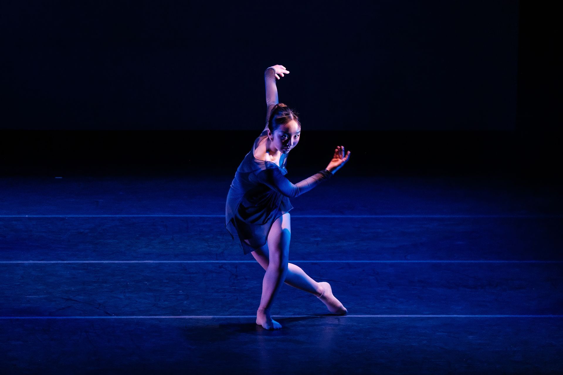 Dancer in a blue costume posing on a dark stage under blue lighting