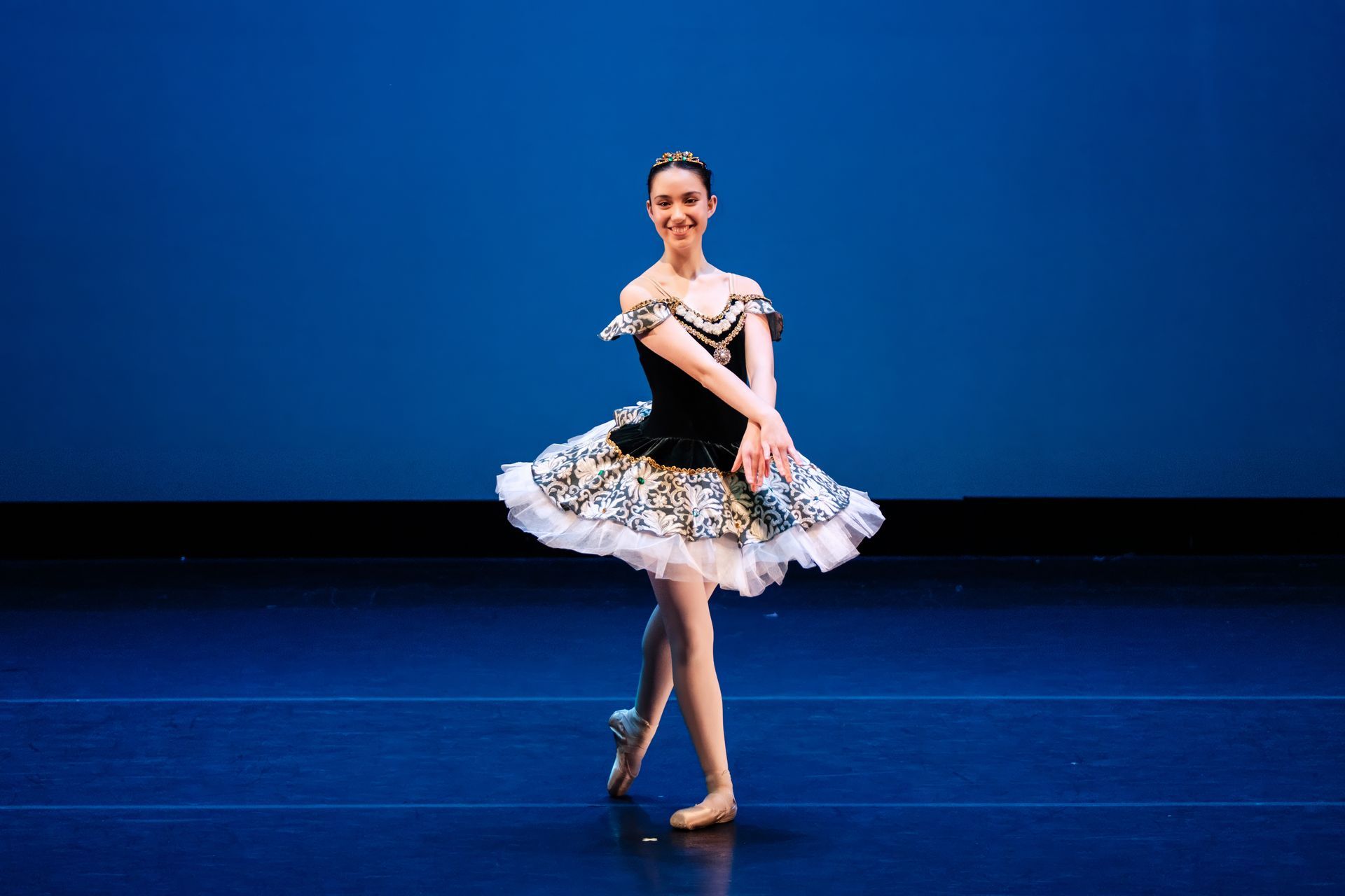 Ballet dancer in a black-and-white tutu performs on a blue-lit stage