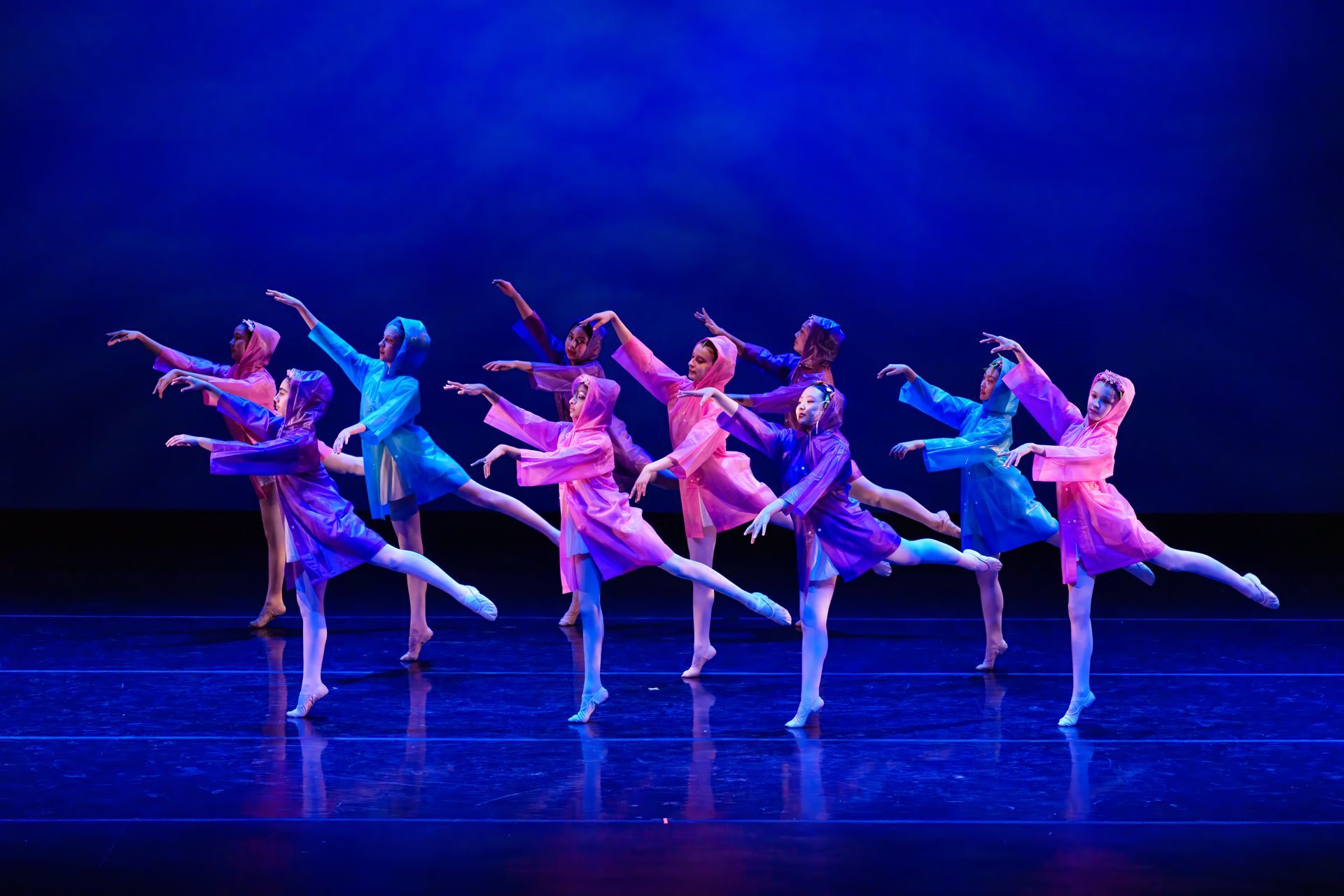Ballet dancers in pink and blue costumes perform synchronized poses on a blue-lit stage