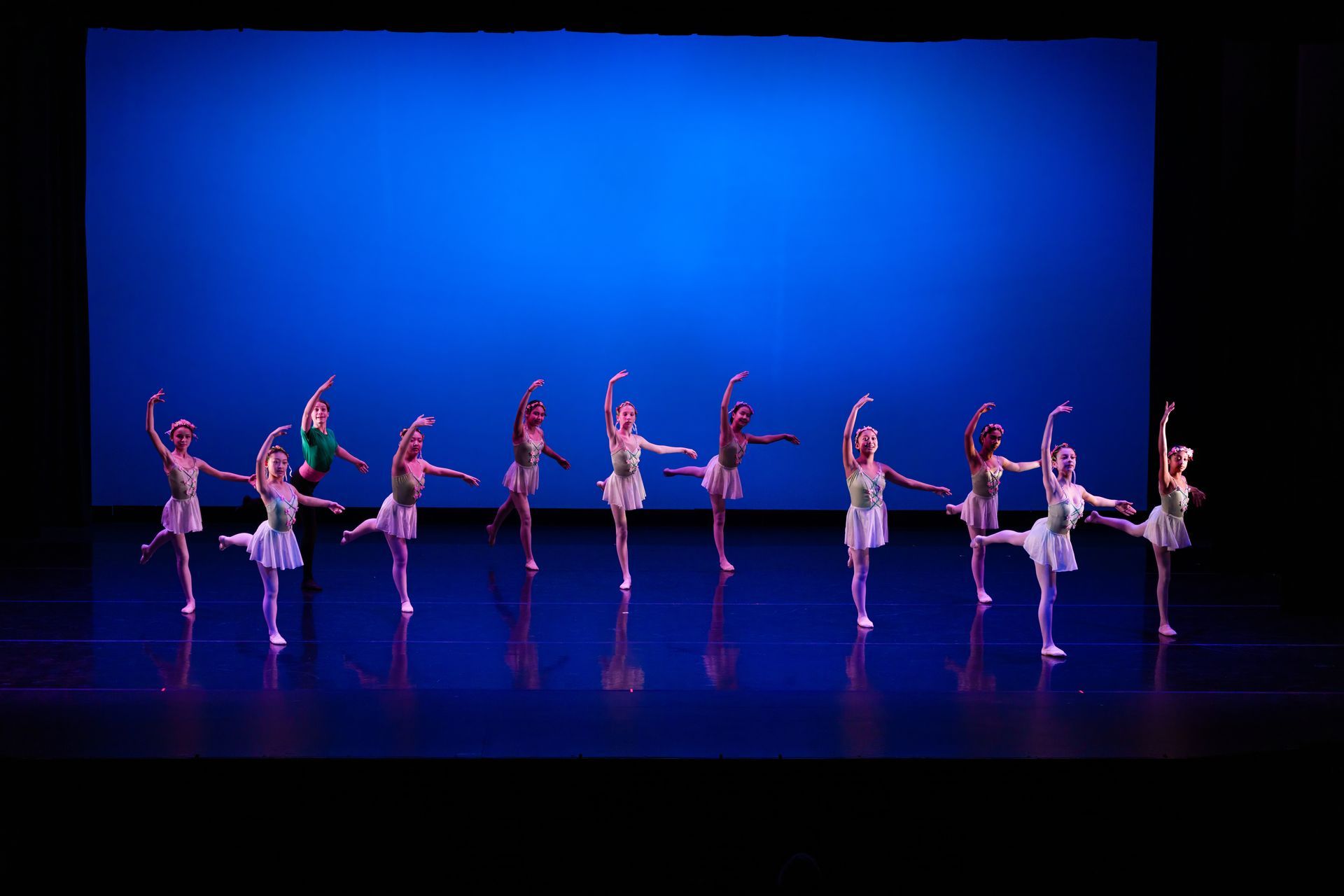 Ballet dancers in white costumes pose in a line on a blue-lit stage