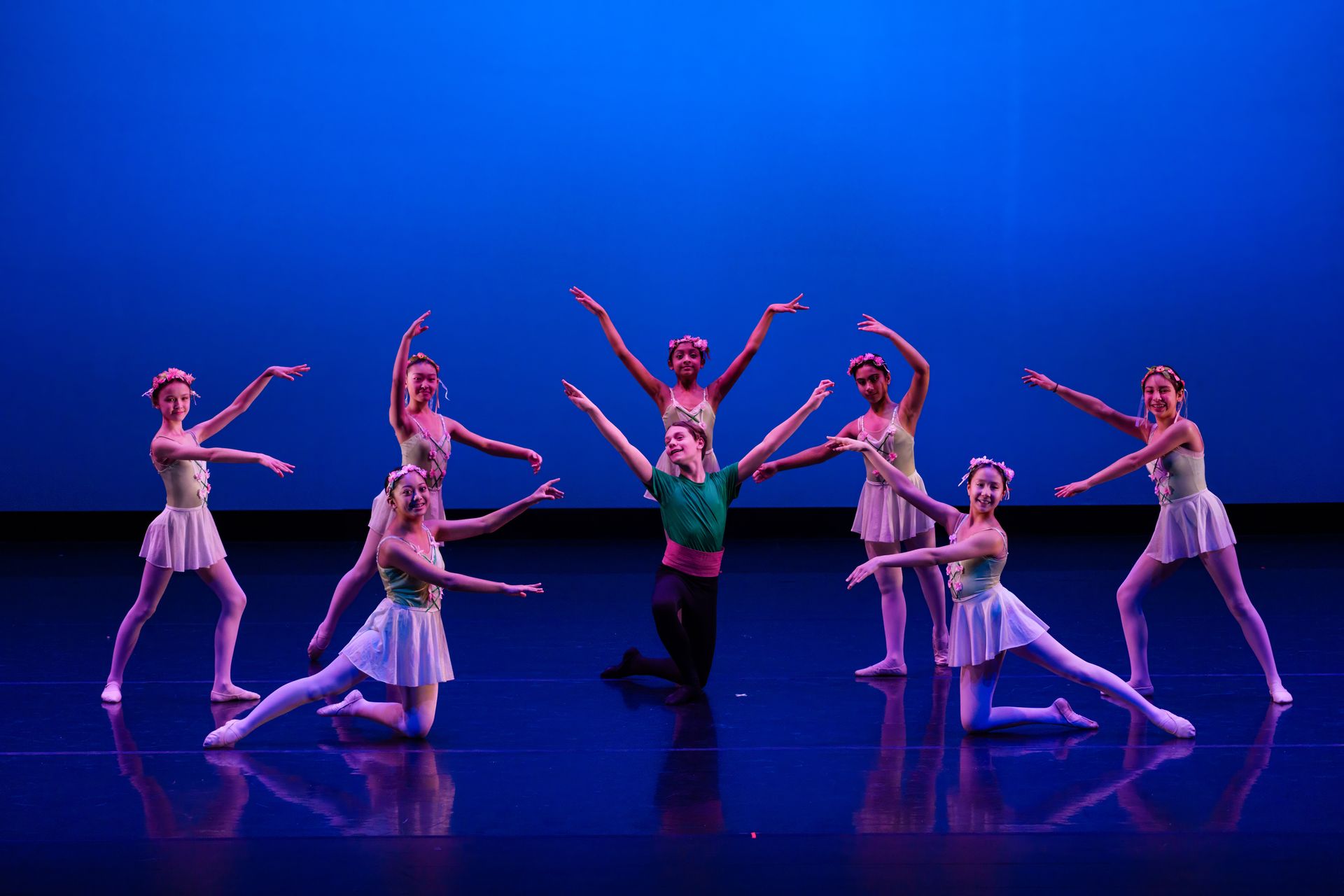 Ballet dancers posing in colorful costumes on a blue-lit stage