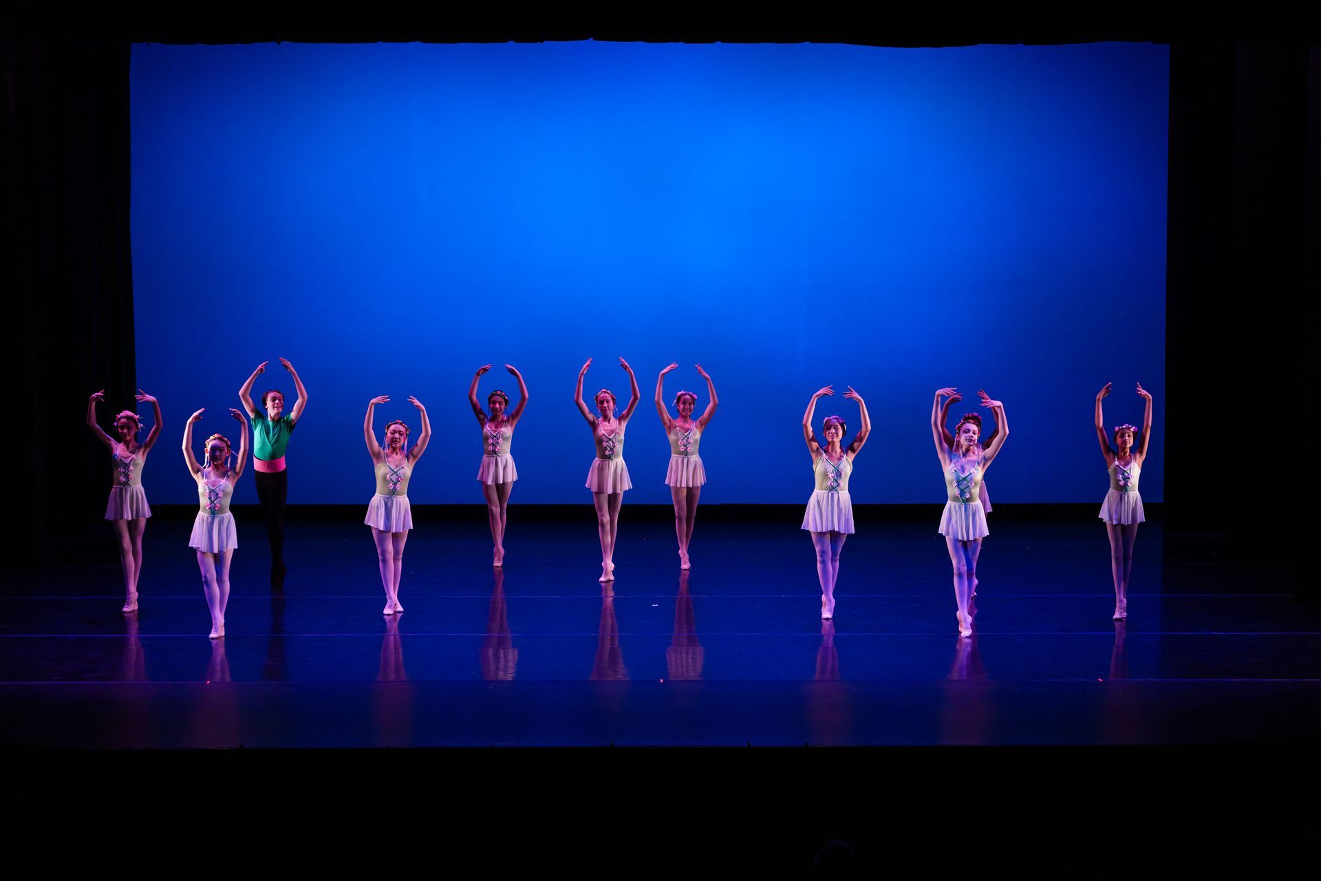 Ballet dancers in colorful costumes pose across a blue-lit stage with arms raised.