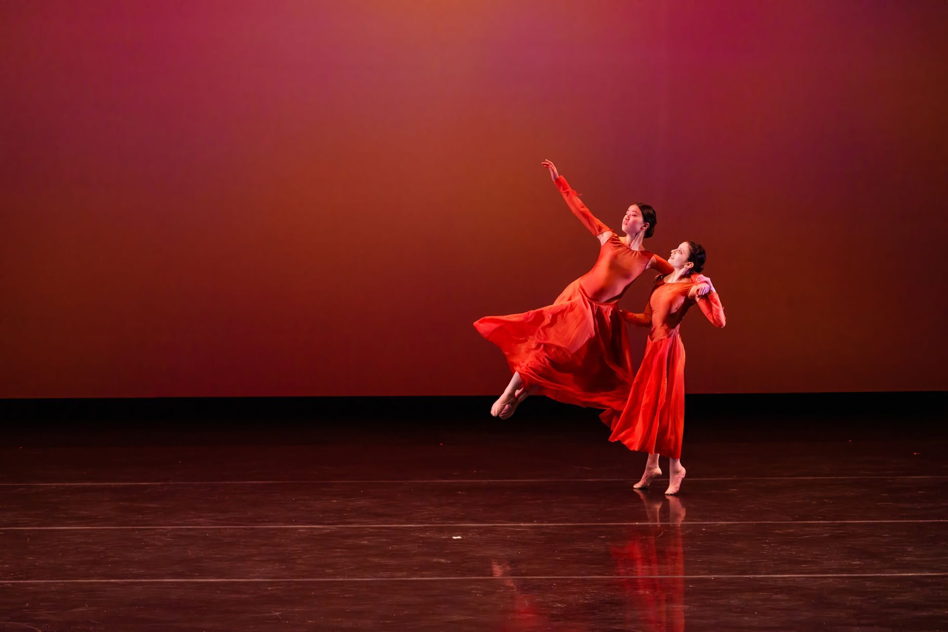 Two dancers in red perform a graceful lift on a dark stage with a red backdrop