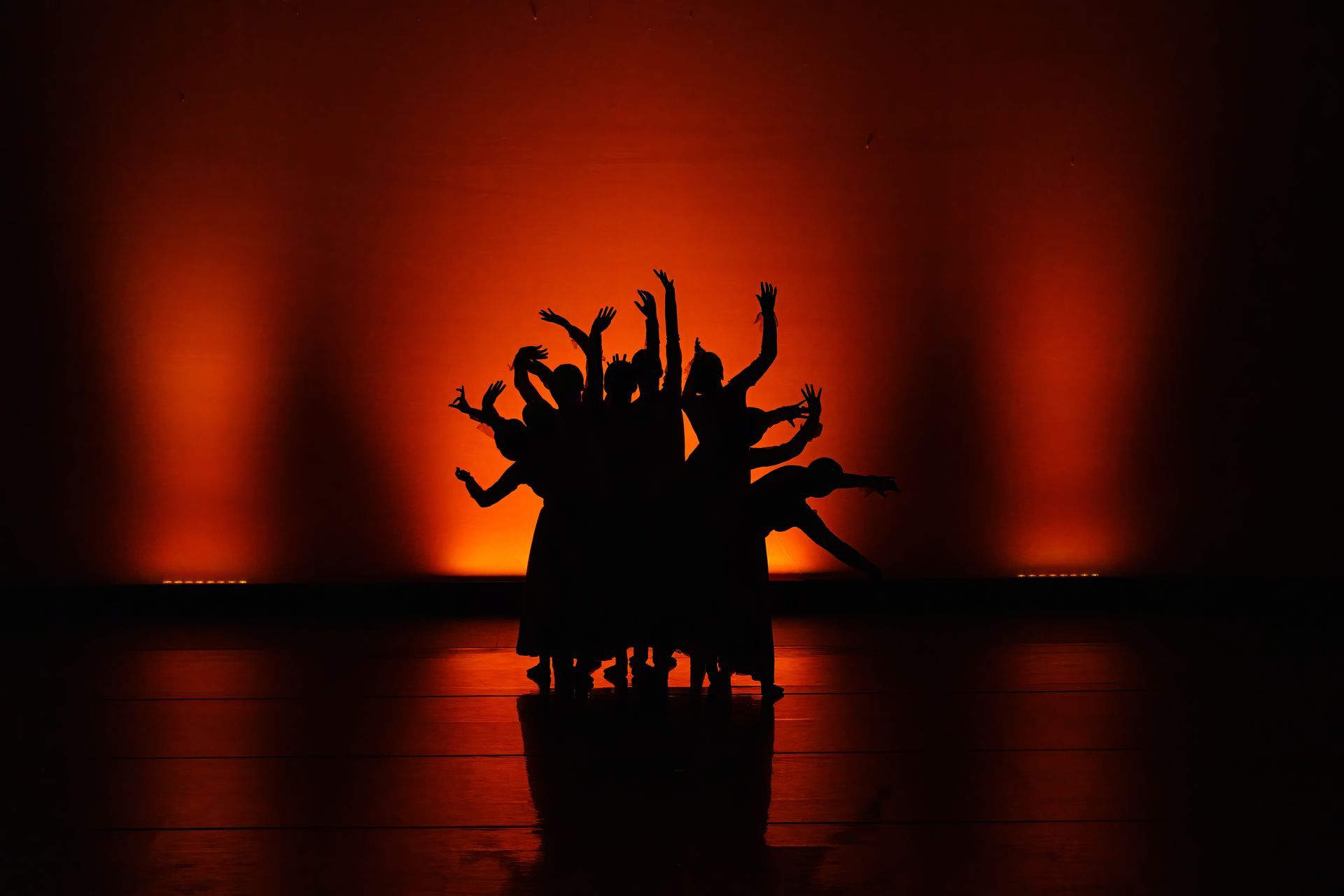 Silhouette of a spiky sculpture on a reflective floor, lit by red-orange stage lights