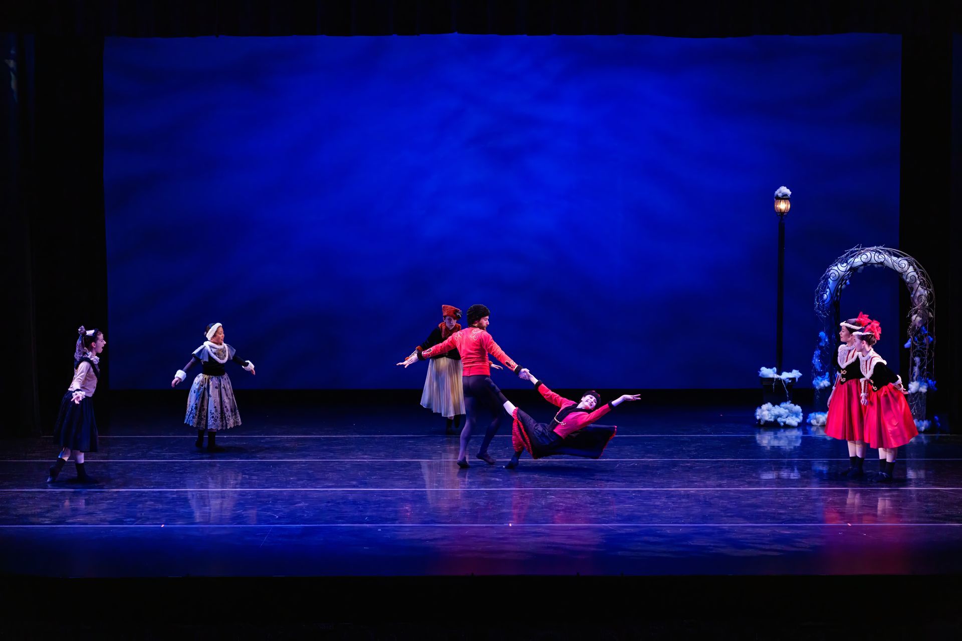 Theater stage with dancers in red and white costumes under blue lighting, mid-performance.