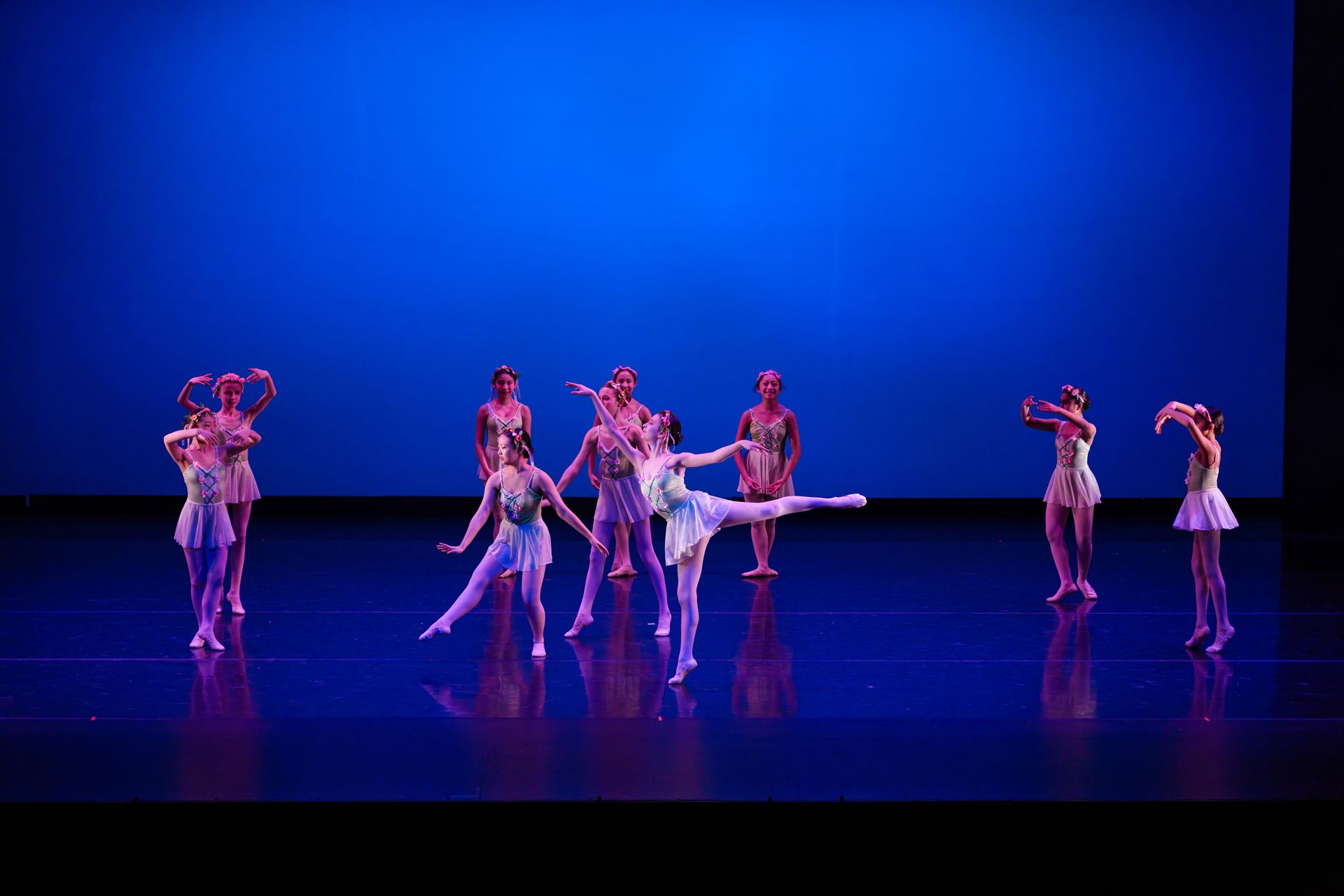 Ballet dancers in white costumes perform on a blue-lit stage
