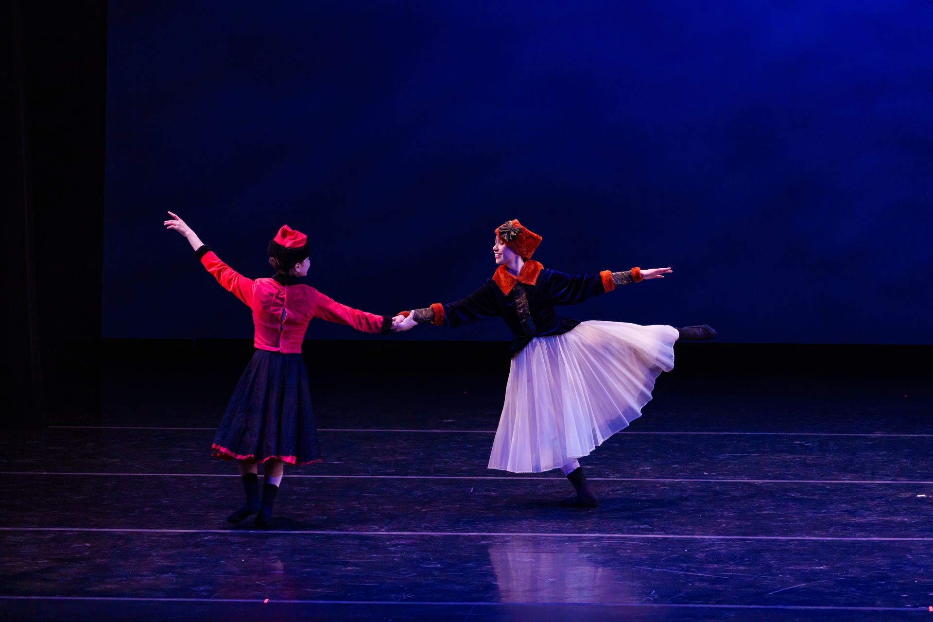 Two dancers in black and white costumes pose on a dark stage with blue lighting.