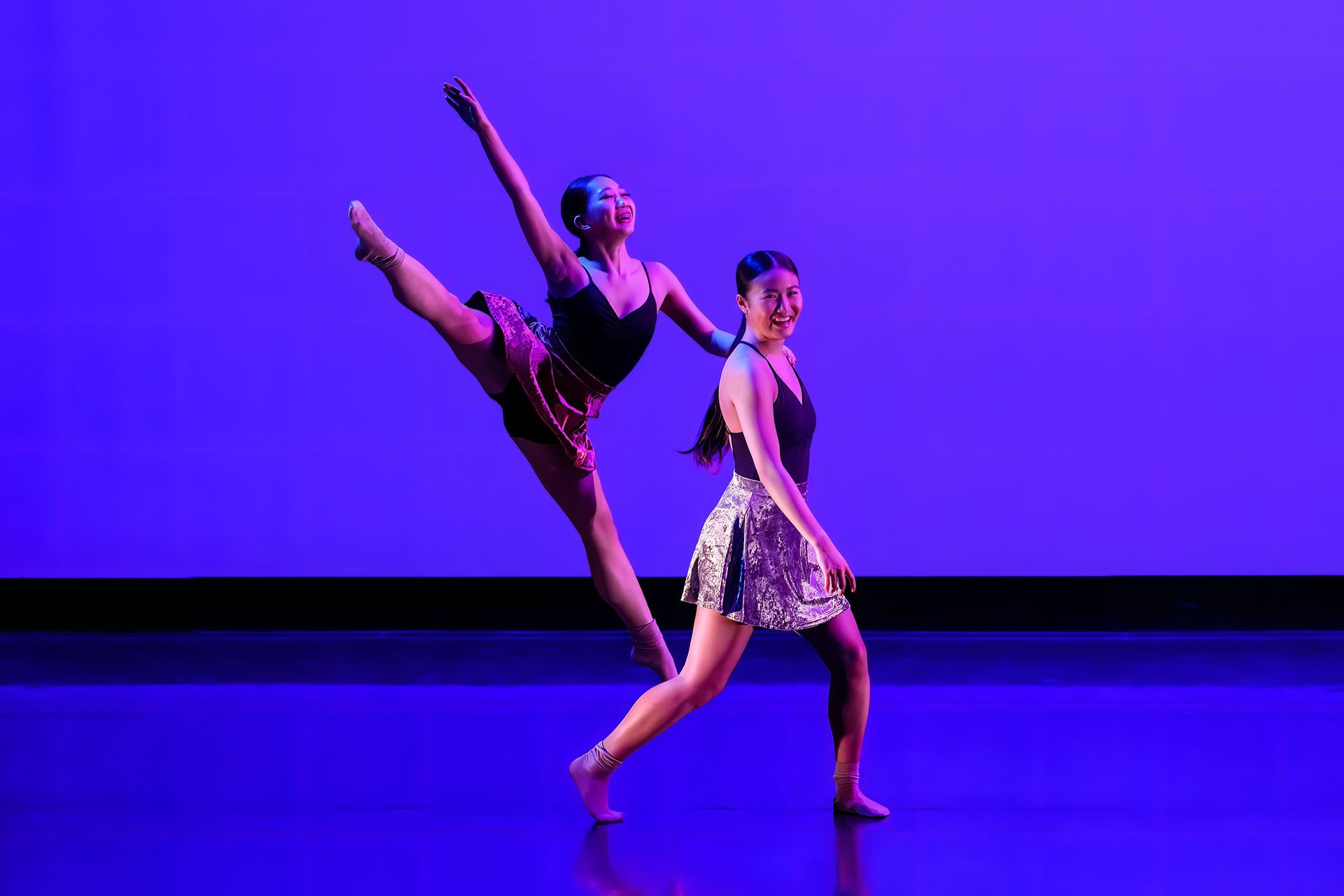 Two dancers performing a ballet pose on a purple-lit stage