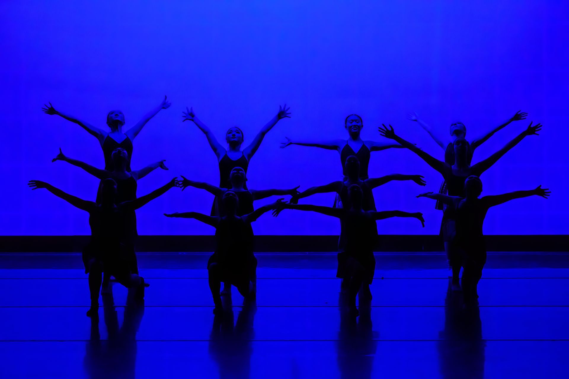 Silhouetted dancers with arms raised on a blue-lit stage.
