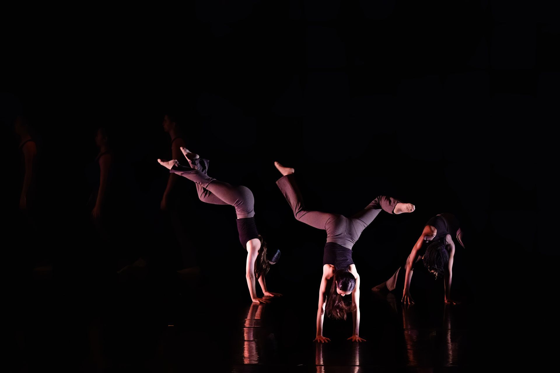 Dancers in dark clothing performing acrobatic poses on a dimly lit stage with red reflections