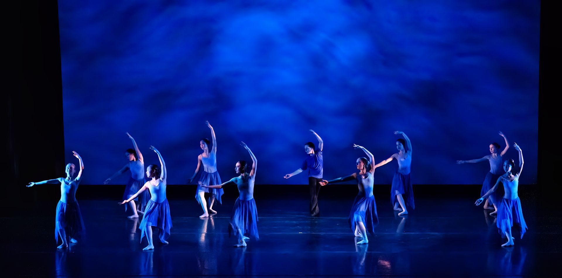 Ballet dancers in white costumes performing on a blue-lit stage