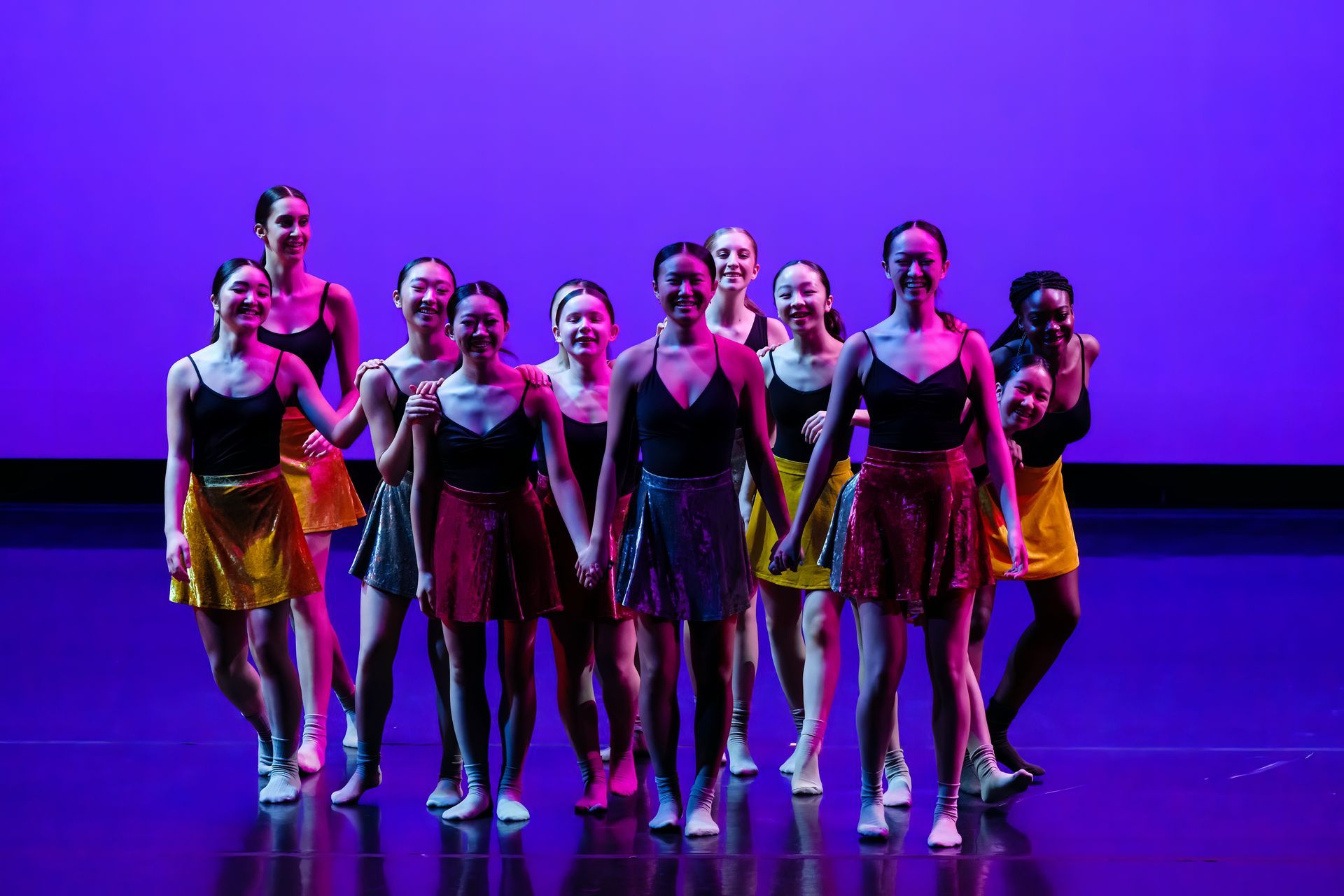 Group of dancers posing on a purple-lit stage in colorful costumes