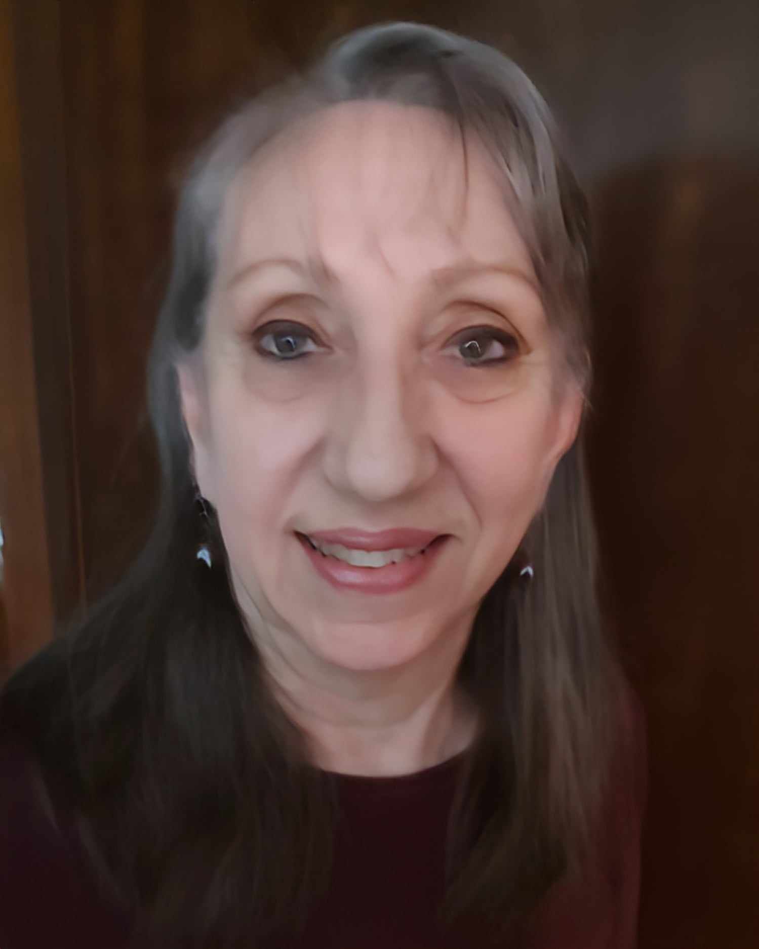 Smiling woman with long gray hair wearing earrings against a dark background