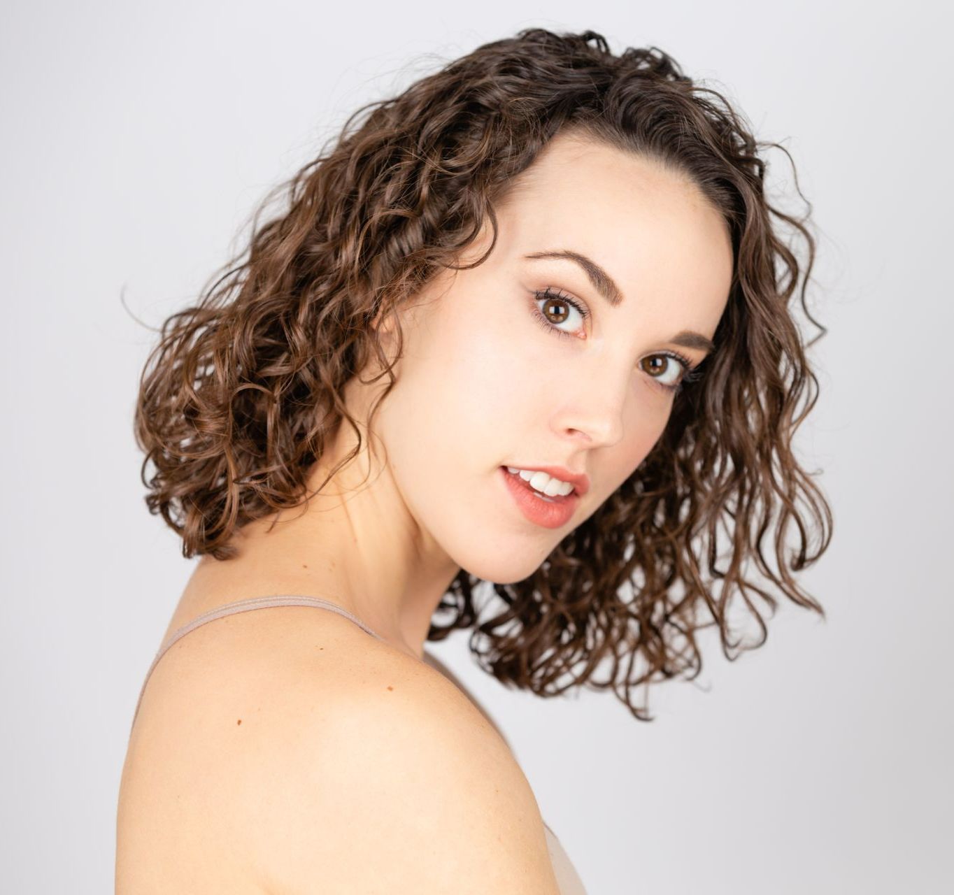 Portrait of a curly-haired person looking over a shoulder against a light gray background