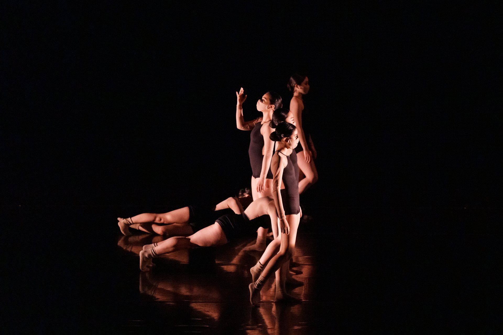 Three dancers in dramatic poses on a dark stage, lit with warm amber light and reflected on the floor