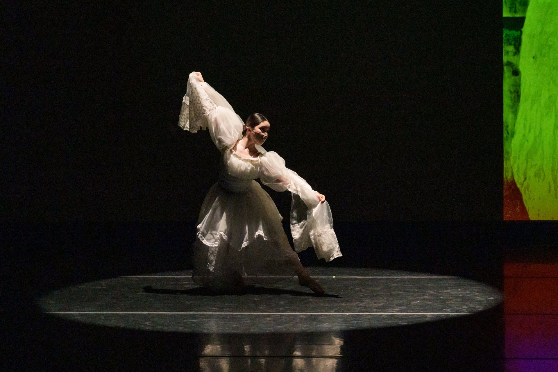 Dancer in a white flowing costume posing on a dark stage under a spotlight