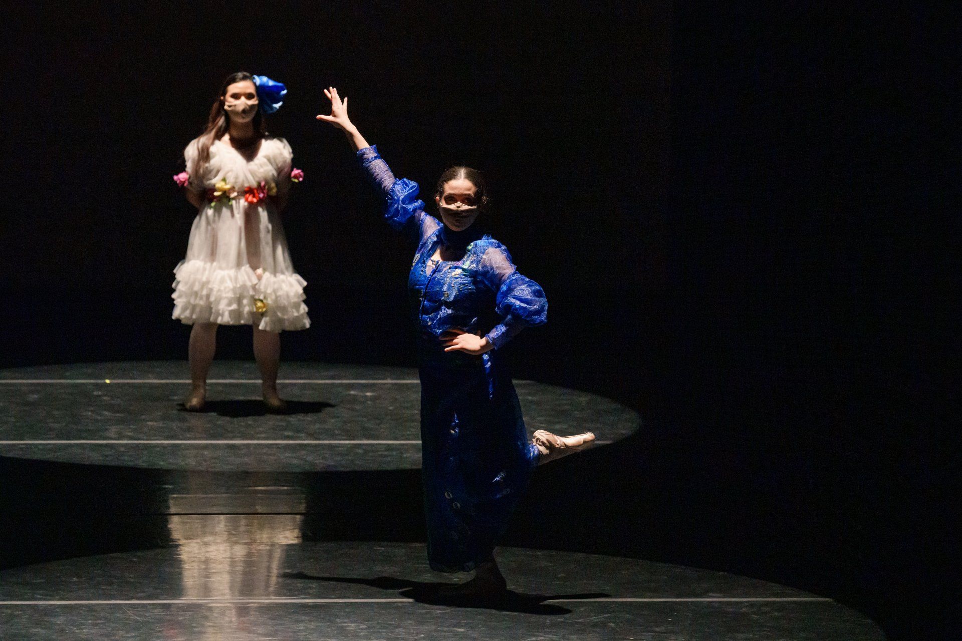 Two performers on a dark stage, one in white and one in blue, striking expressive poses under spotlights