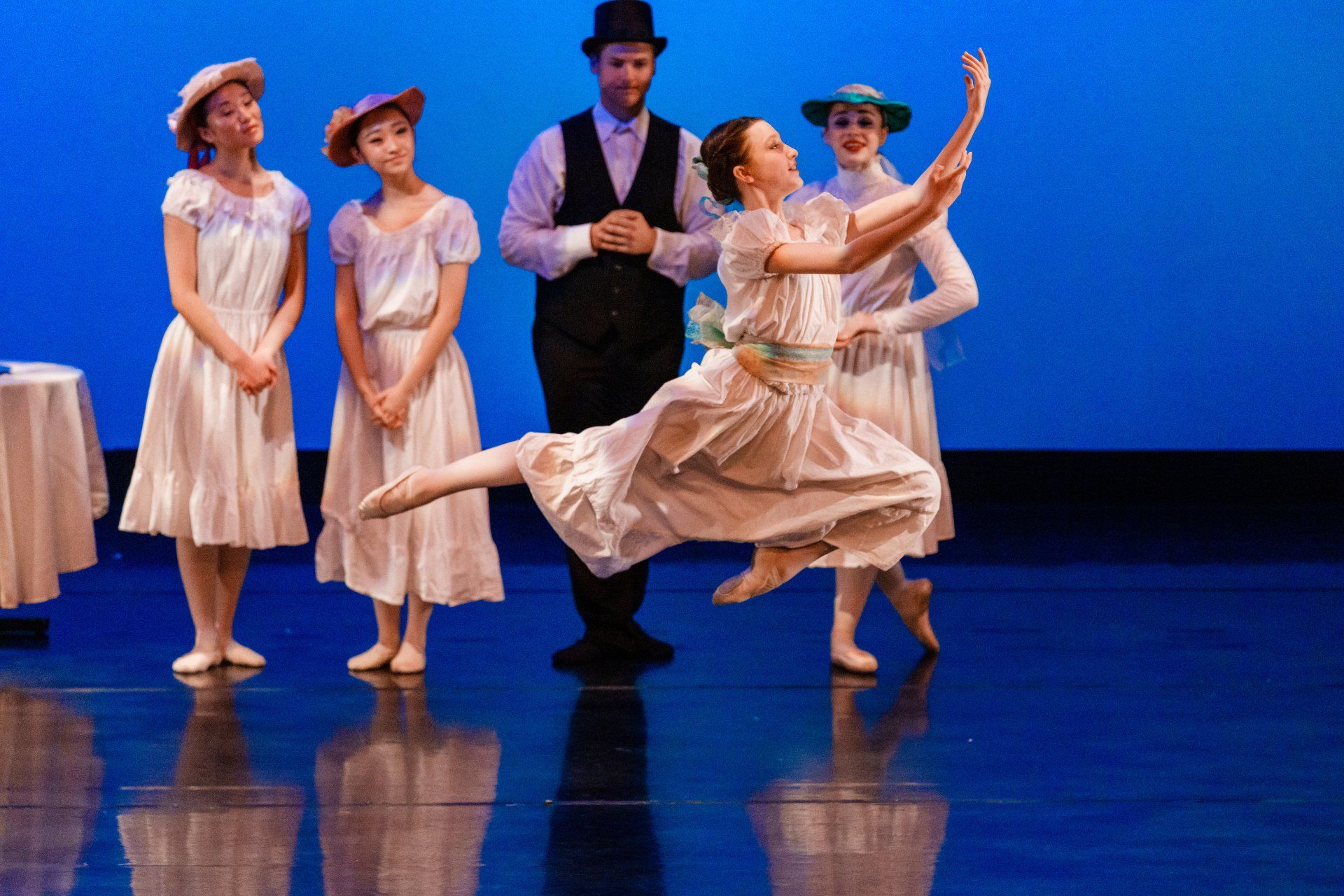 Five dancers in pastel costumes pose and dance on a glossy blue stage