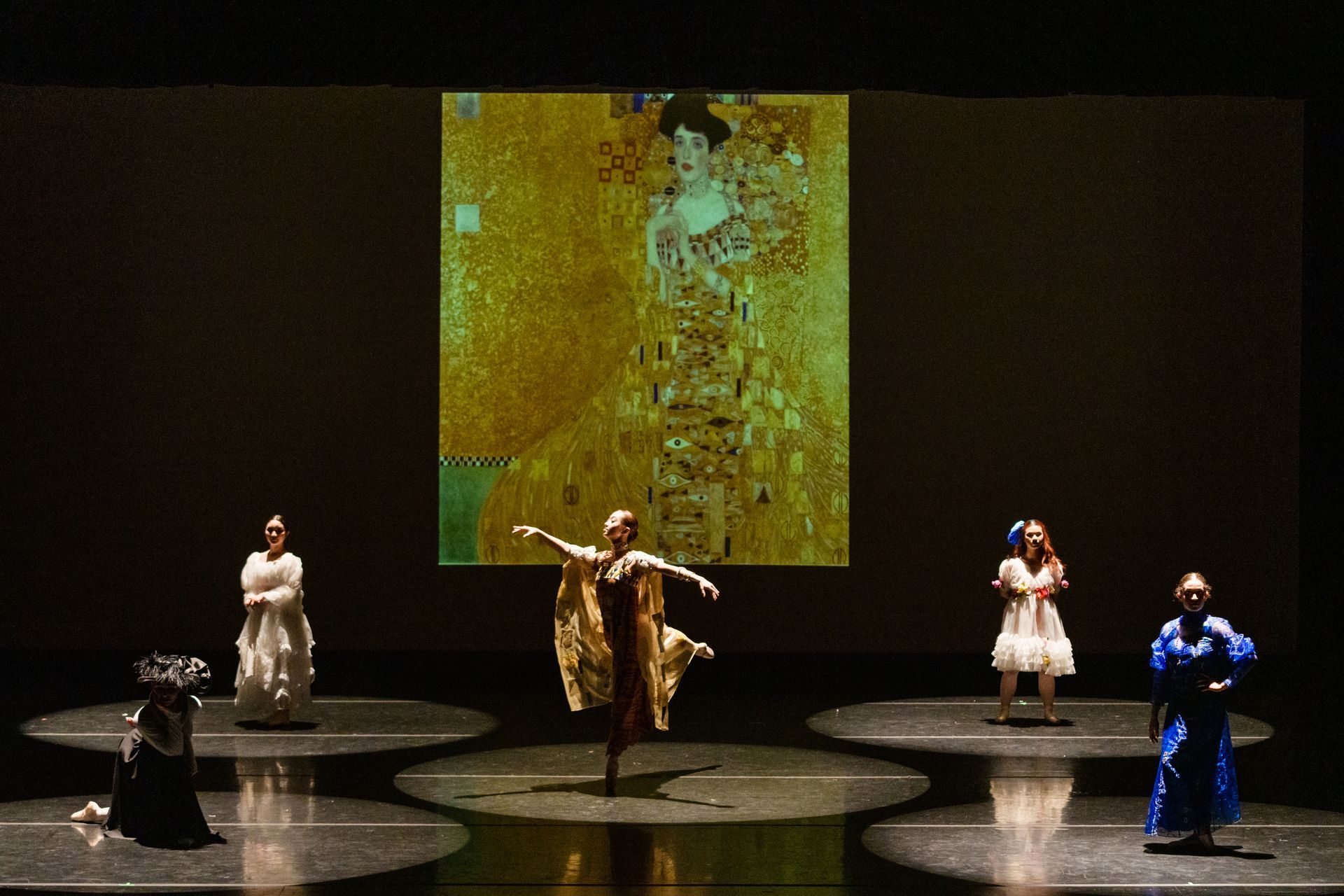 Five performers on a dark stage beneath a glowing abstract projection