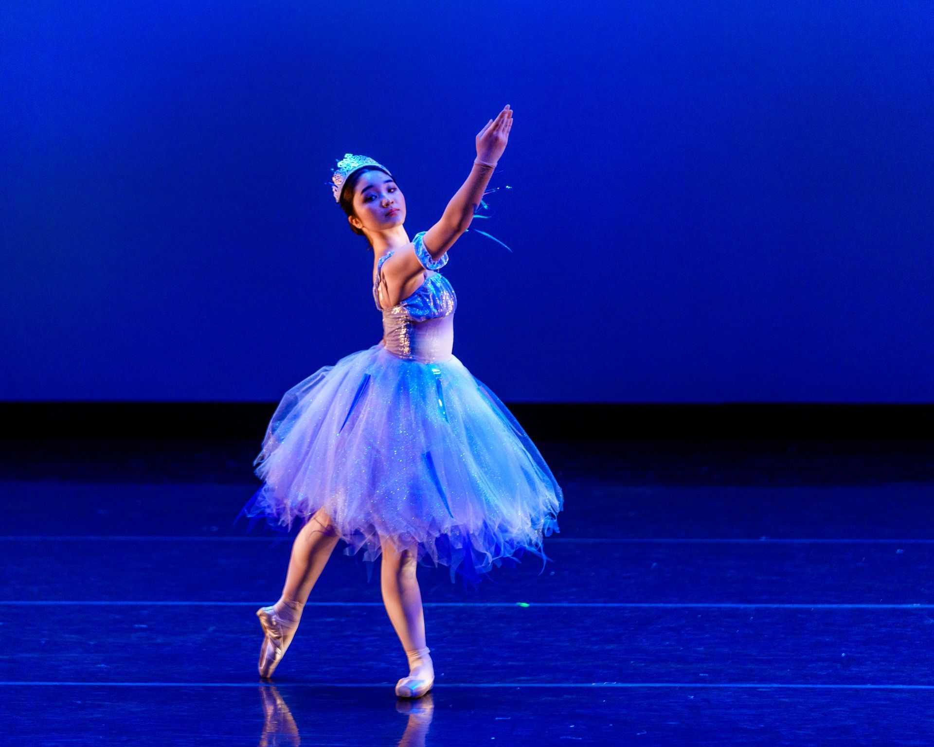 Ballet dancer in a blue tutu posing on a stage under blue lighting