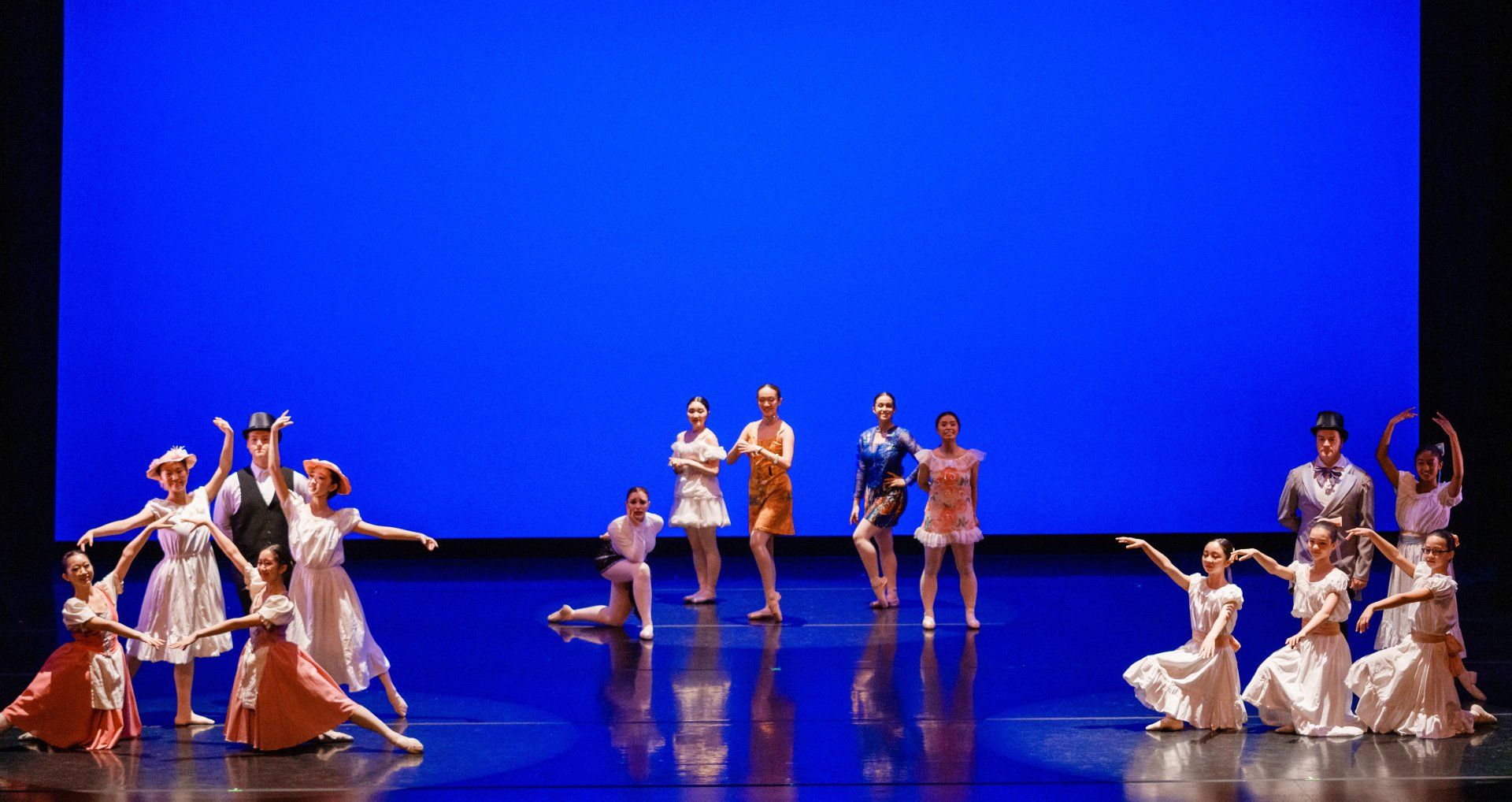 Dance performers in colorful costumes on a stage with a bright blue backdrop