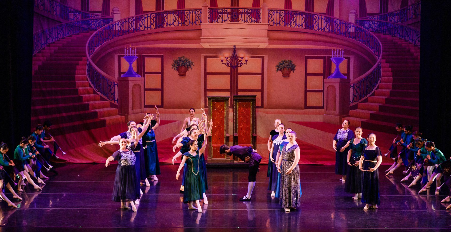 A stage dance performance in a grand theater, with performers in colorful costumes under pink-purple lighting.