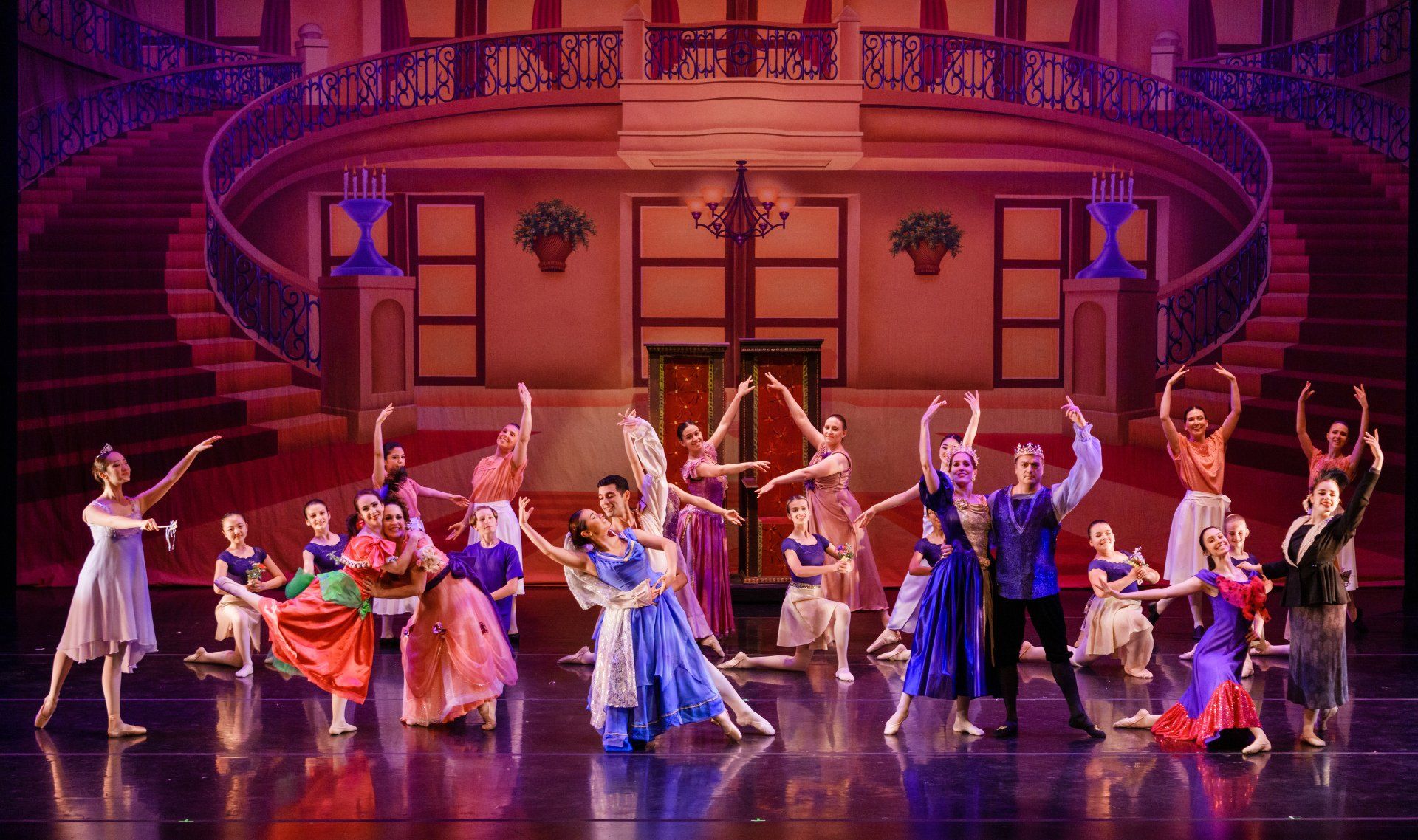 Costumed dancers perform on a grand theater stage with a pink-lit staircase and ornate backdrop.