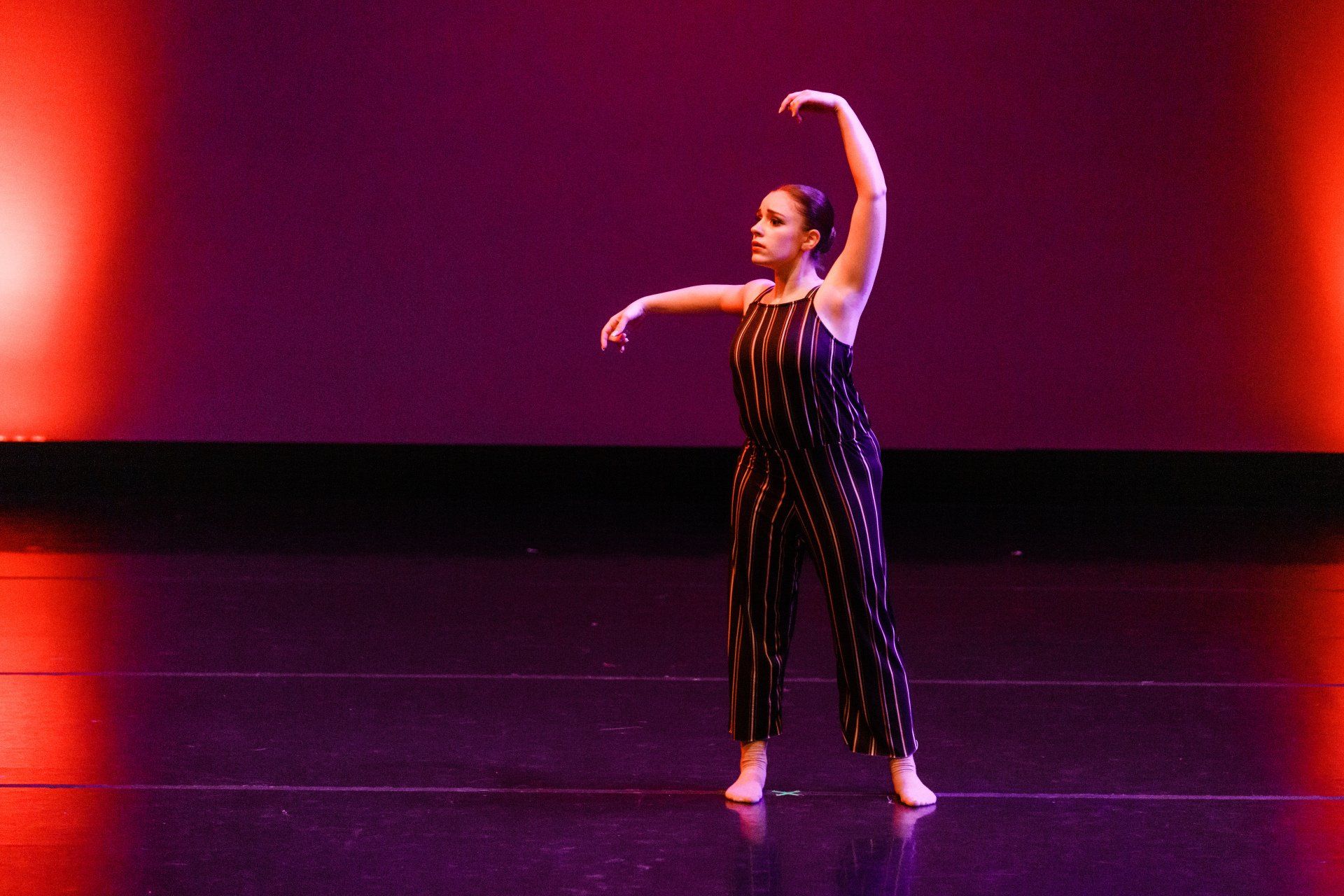 Dancer in a black striped jumpsuit posing on a lit stage with one arm raised