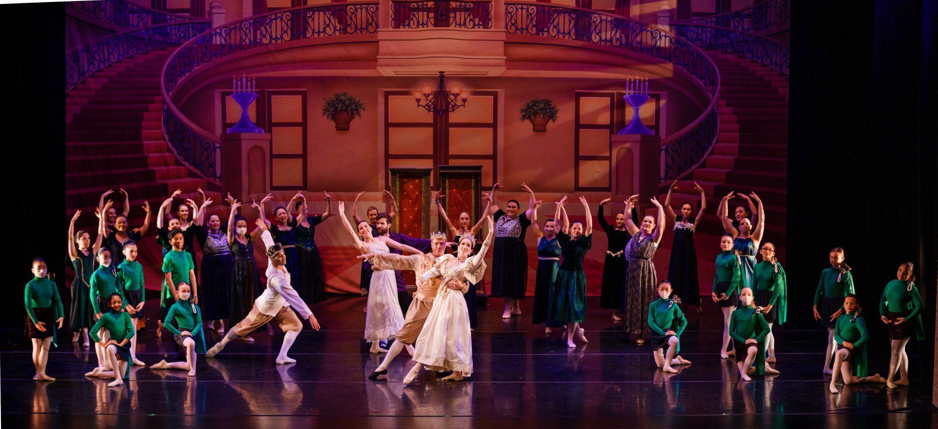 Theater stage with dancers in green costumes and a central pair in white under warm pink lighting