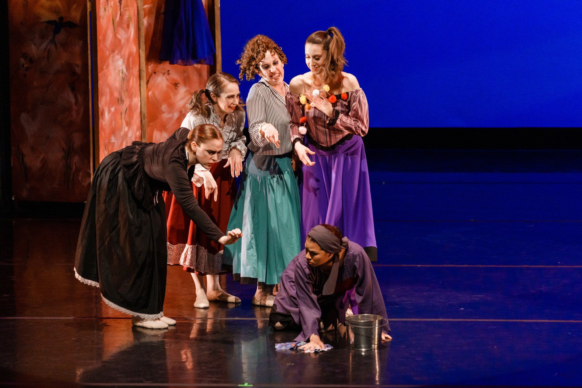 Actors in colorful costumes crouch and stand on a stage during a performance.