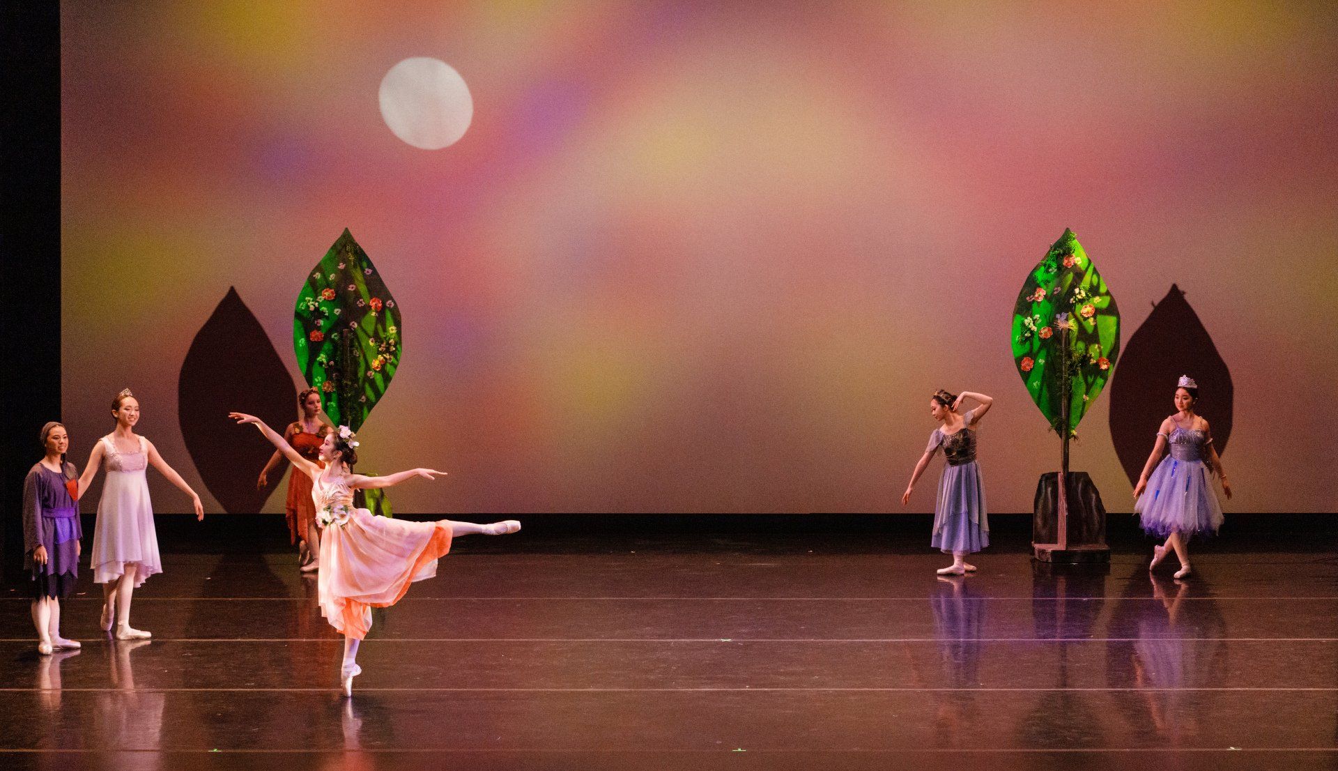 Ballet dancers on a stage with colorful leaf props and soft pink lighting