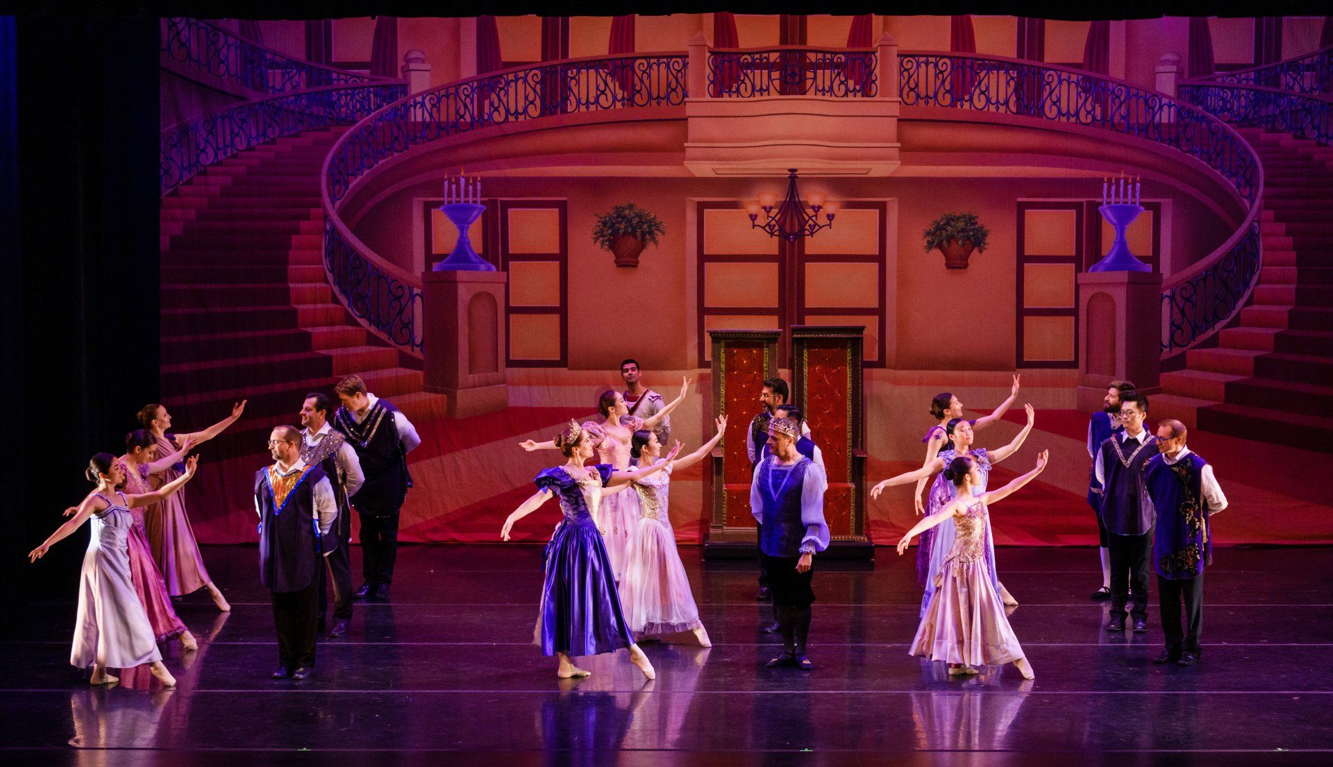 Ballet dancers performing on a theater stage in pastel costumes under purple lighting