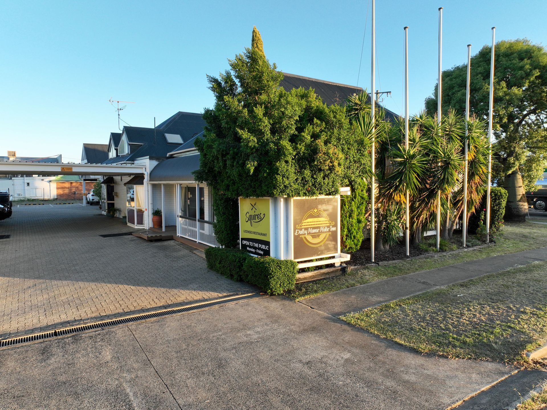 Sunlit entrance to a waterfront building with flags, trees, and a paved path by the water
