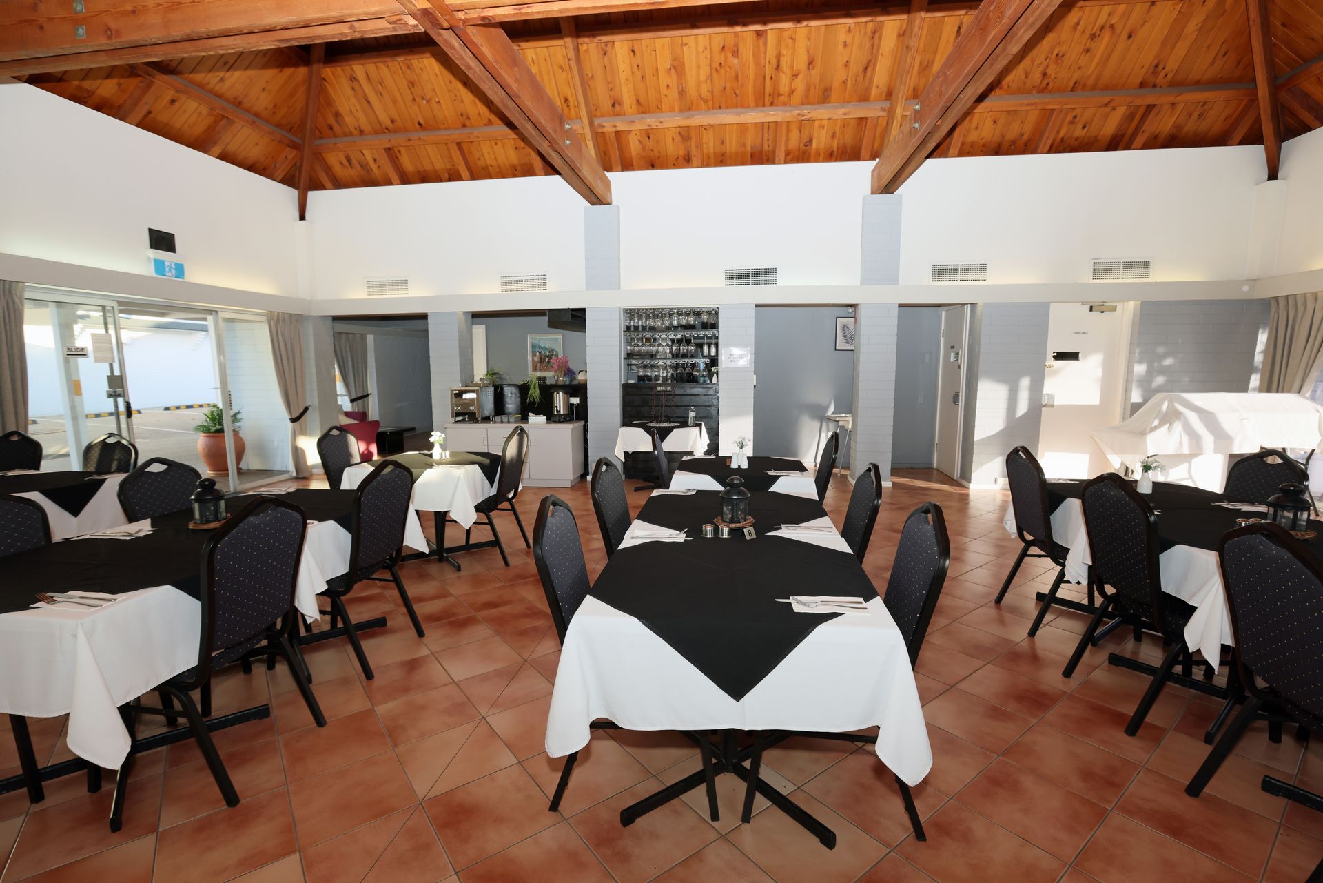 Dining room with black-and-white table settings, black chairs, and a wood-beamed ceiling