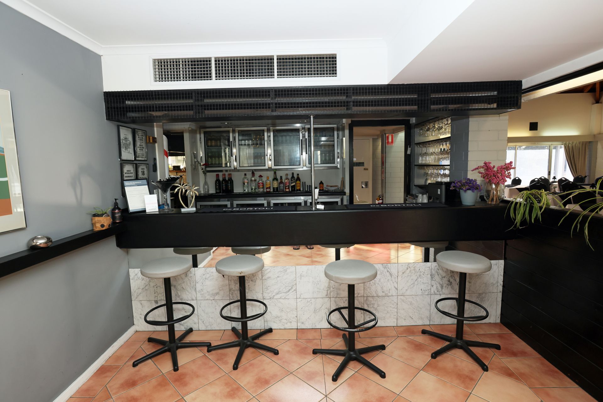 Modern bar interior with black counter, four stools, and a mirrored back bar under bright lighting