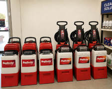 Red industrial floor scrubbers lined up in a store aisle with cleaning supplies in the background