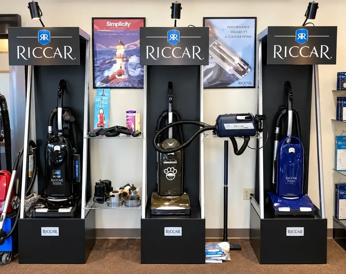 Three Riccar vacuum displays in a showroom, with black, red, and blue models.