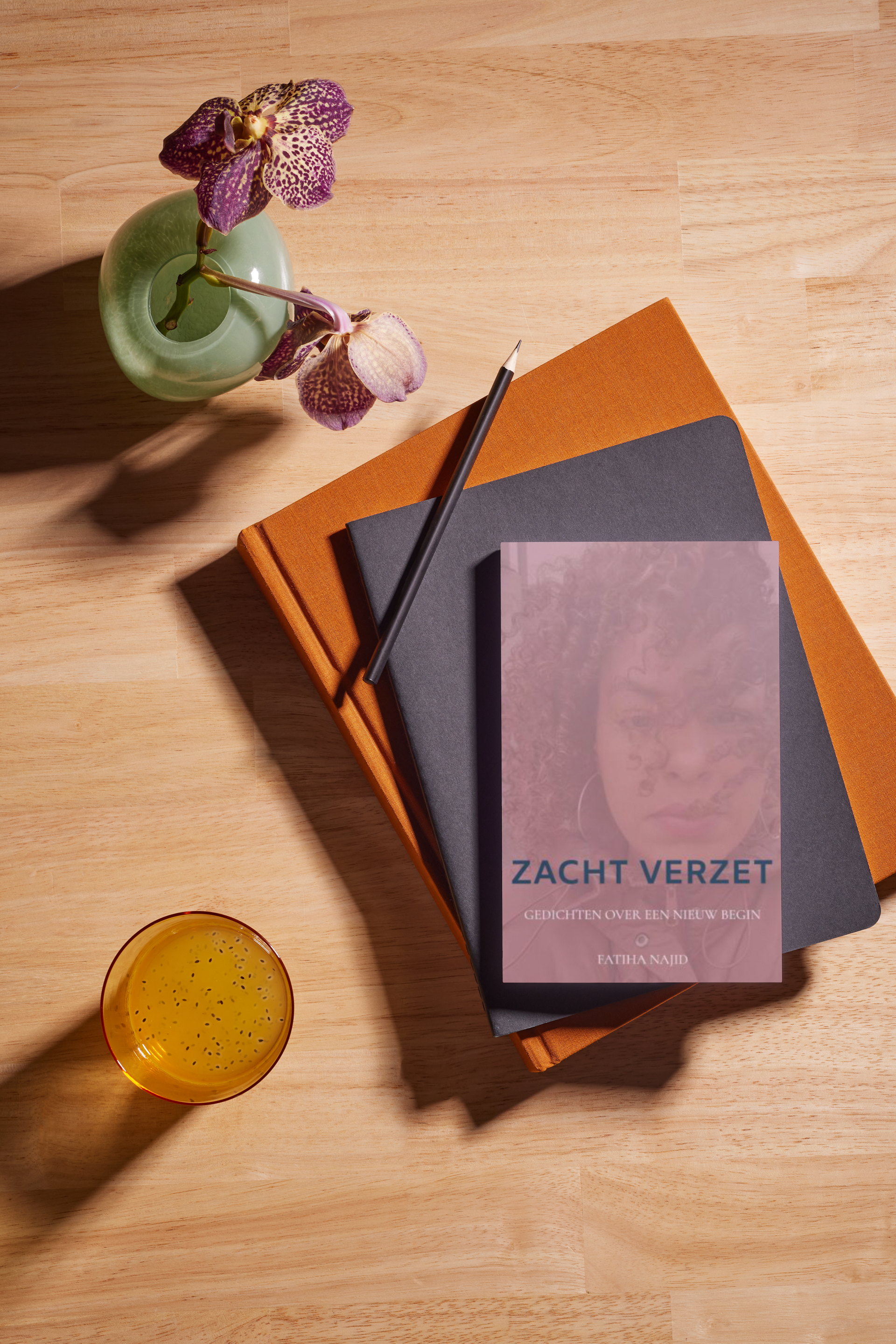 Boek en potlood in een oranje notitieboekje naast een vaas met bloemen op een houten tafel.
