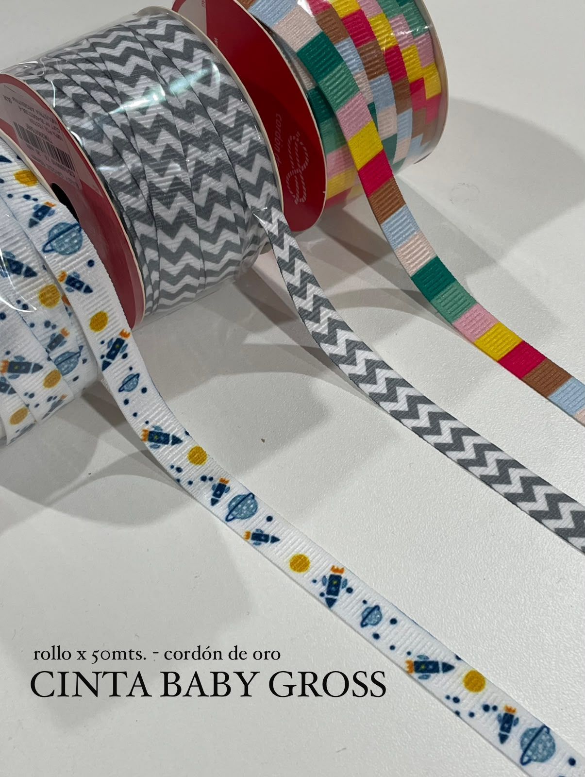 Carrete de cinta con estampados surtidos en gris, blanco, rojo y multicolor, etiquetado como “CINTA BABY GROSS”.
