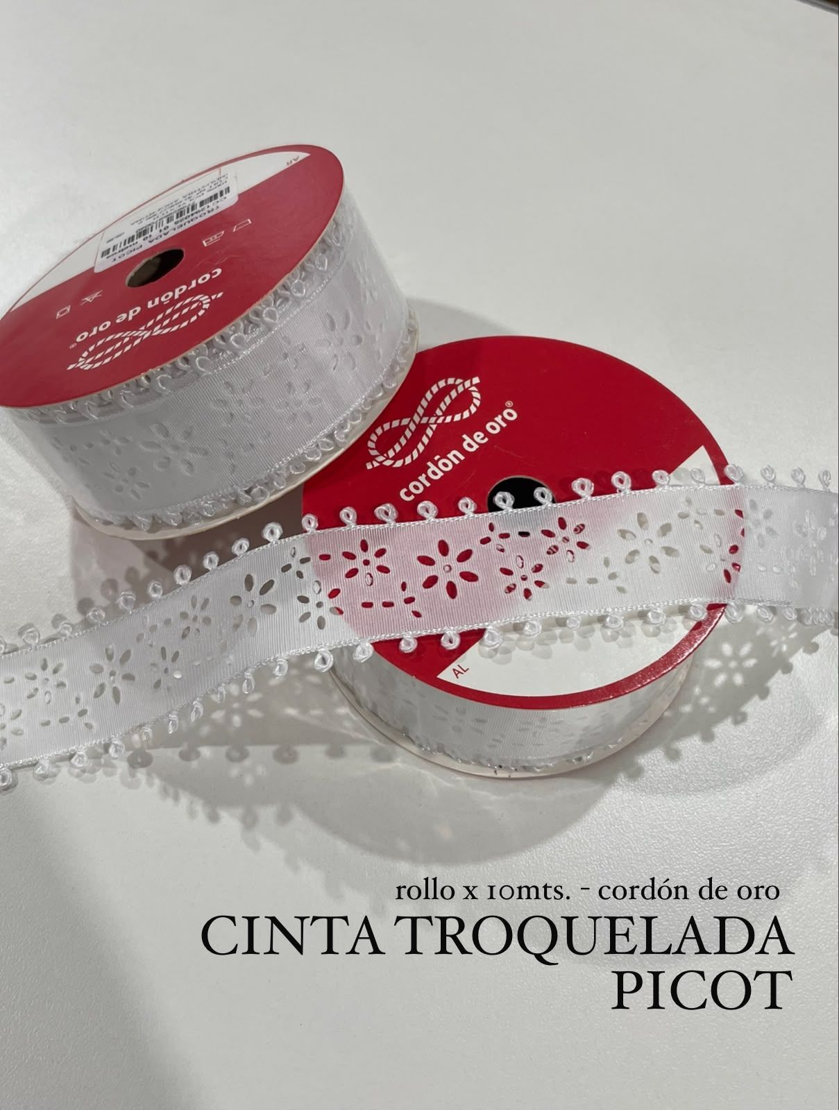 Carrete de cinta de encaje blanco decorativo con etiquetas rojas sobre fondo claro, etiquetado como “cinta troquelada picot”.