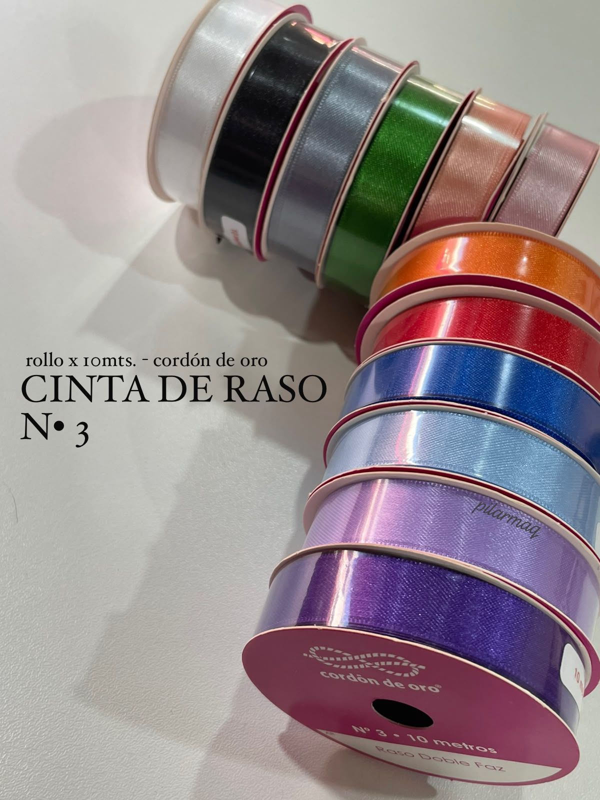Rollos apilados de cinta de satén de varios colores, etiquetados como “Cinta de raso No 3” sobre un fondo blanco.