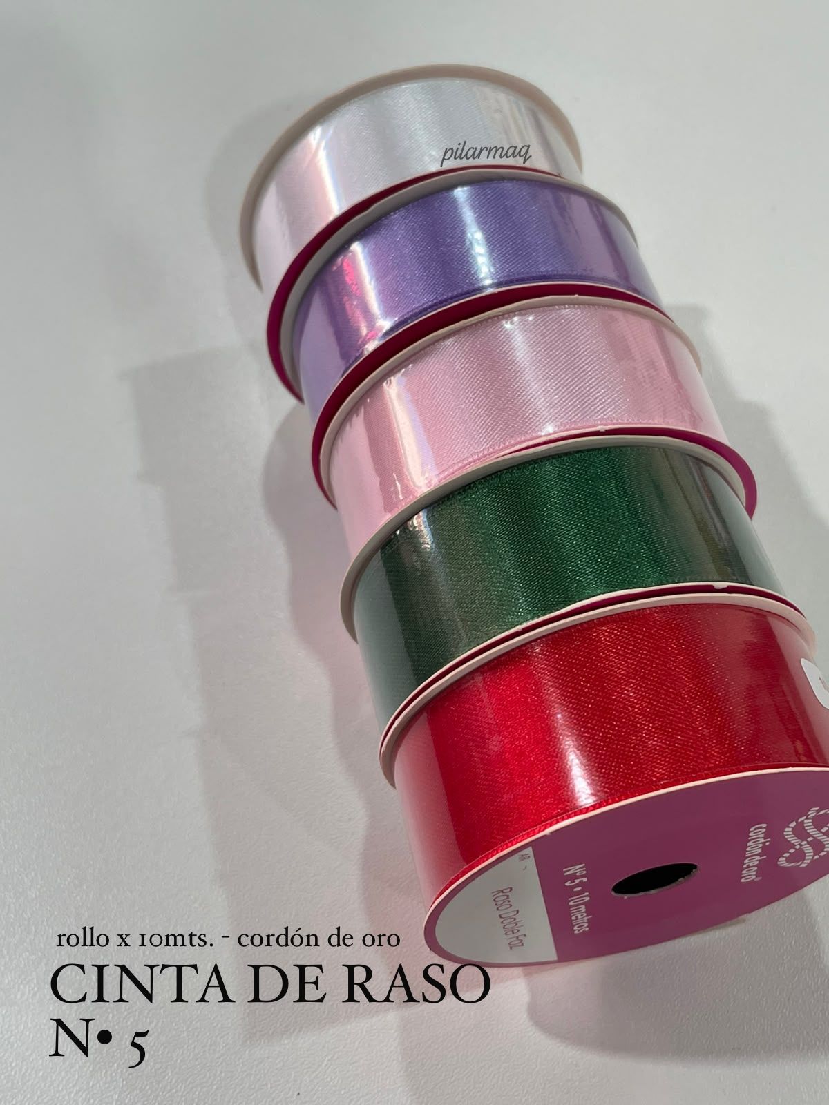 Pila de carretes de cinta de satén de colores: plateado, morado, rosa, verde y rojo sobre un fondo blanco.